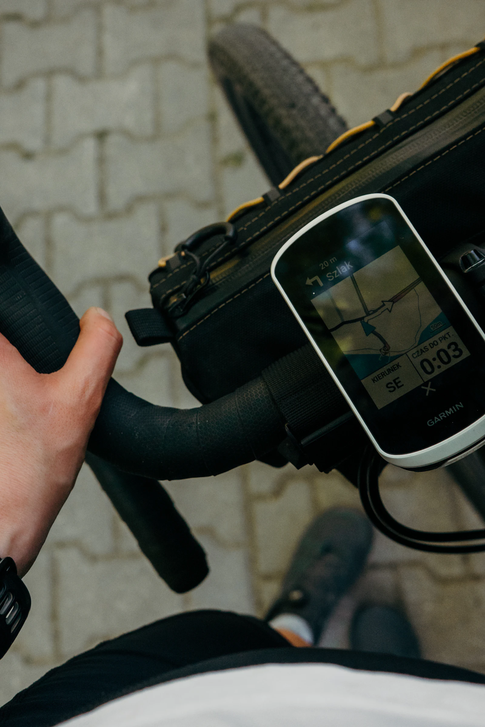 A cyclist's hand on the handlebars next to a GPS unit showing a map