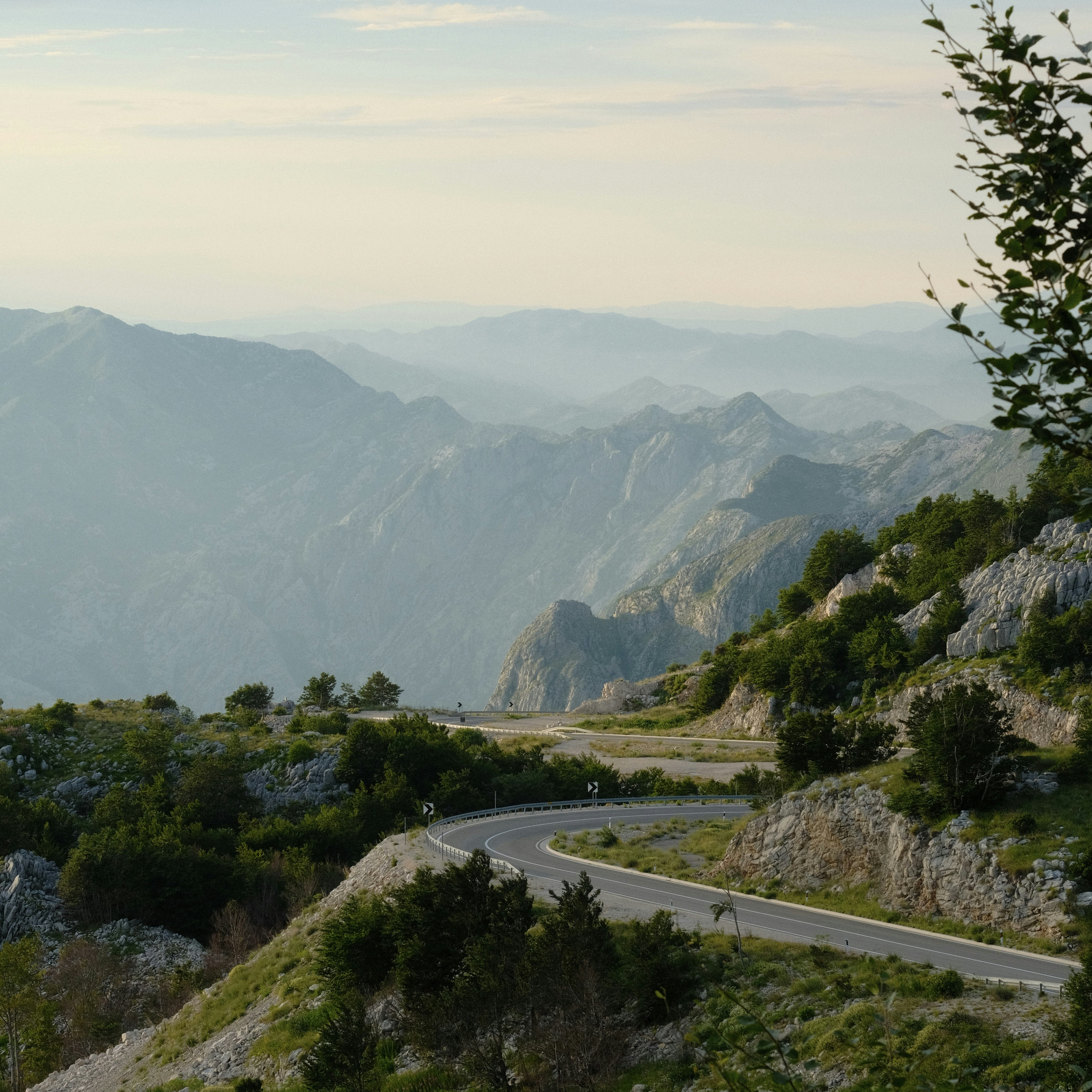 Une route sinueuse grimpe une montagne verte aux sommets brumeux