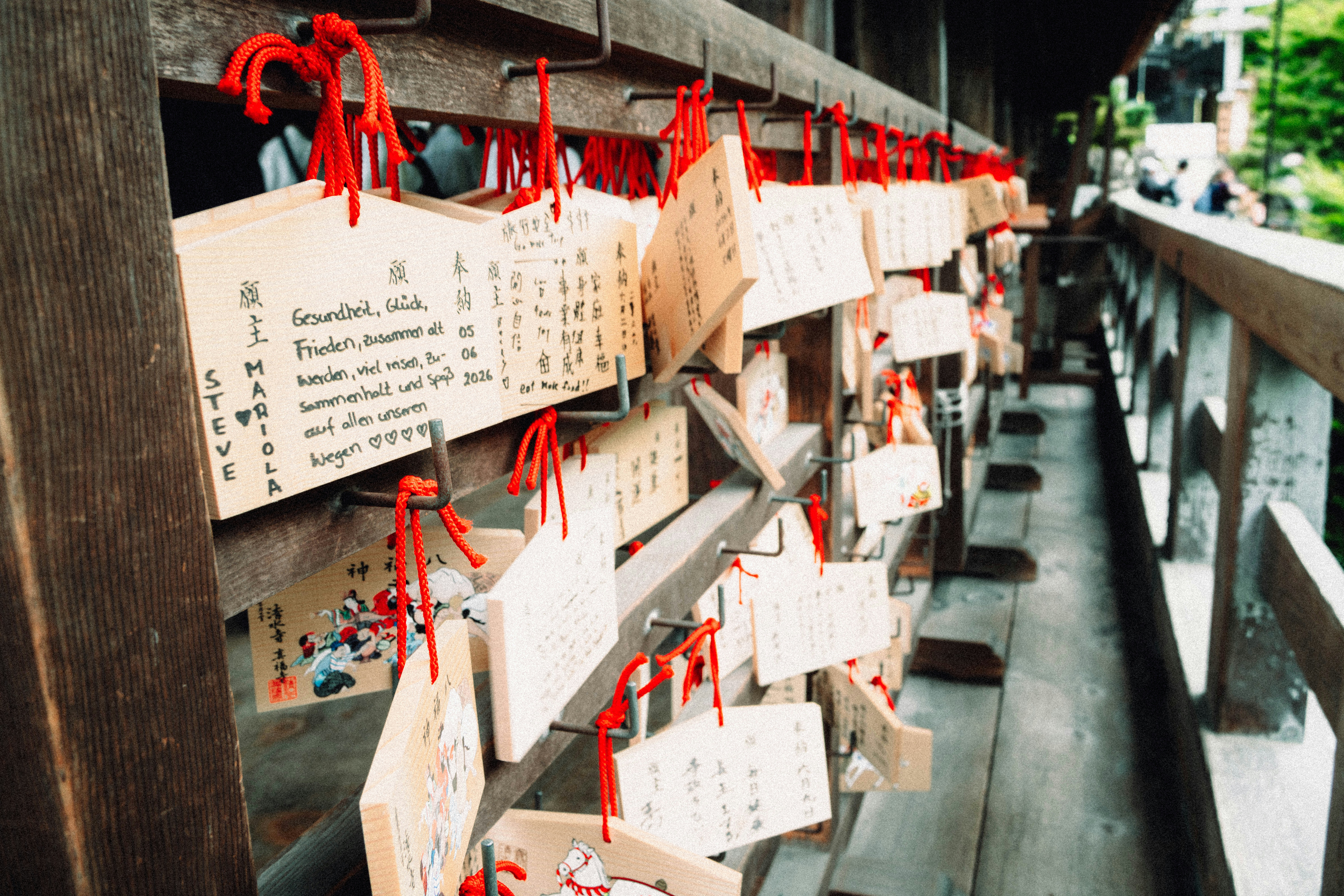 Many wooden japanese prayer plaques hang from a temple railing.
