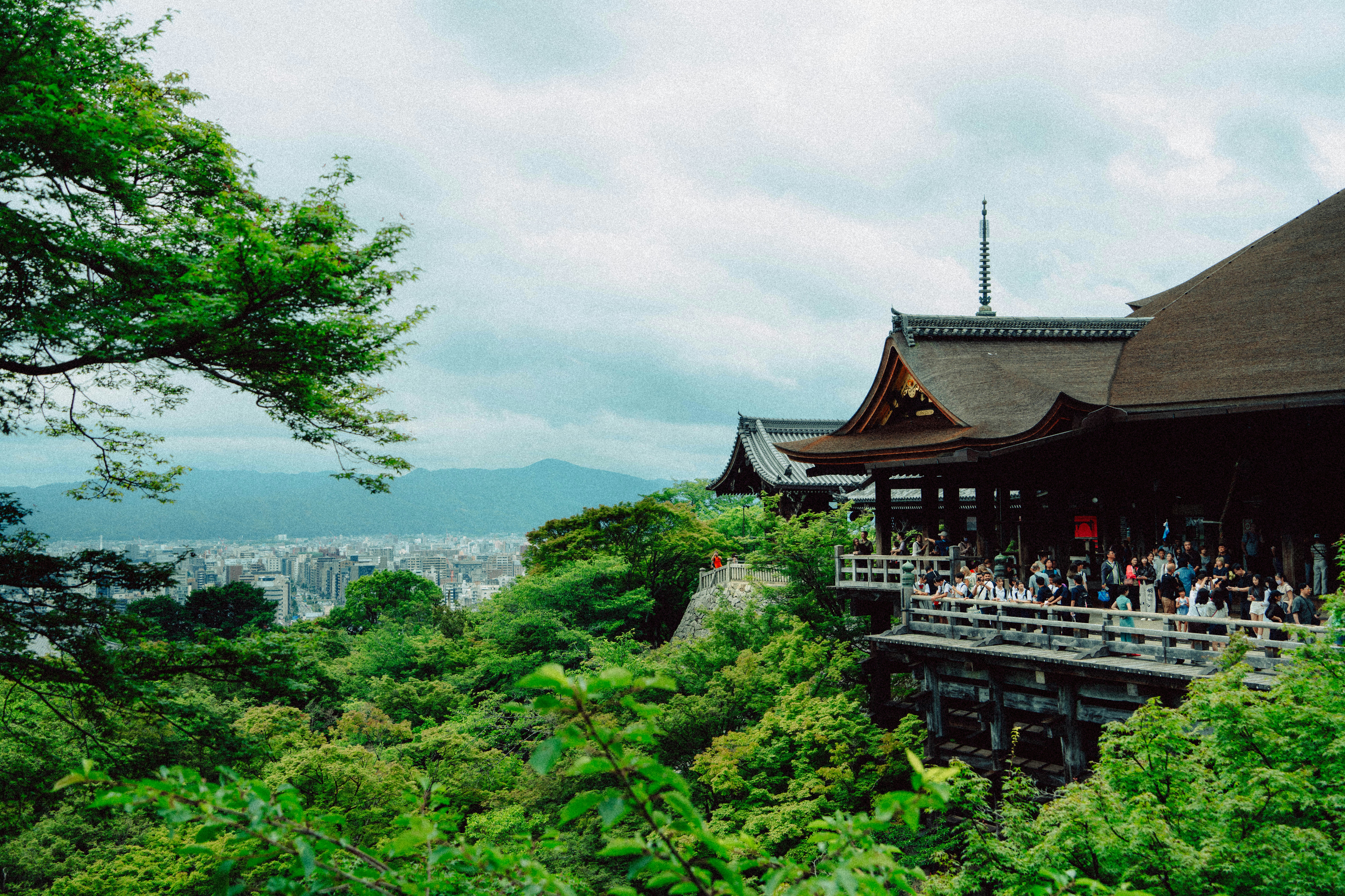 Crowded japanese temple balcony overlooking a city and green hills.
