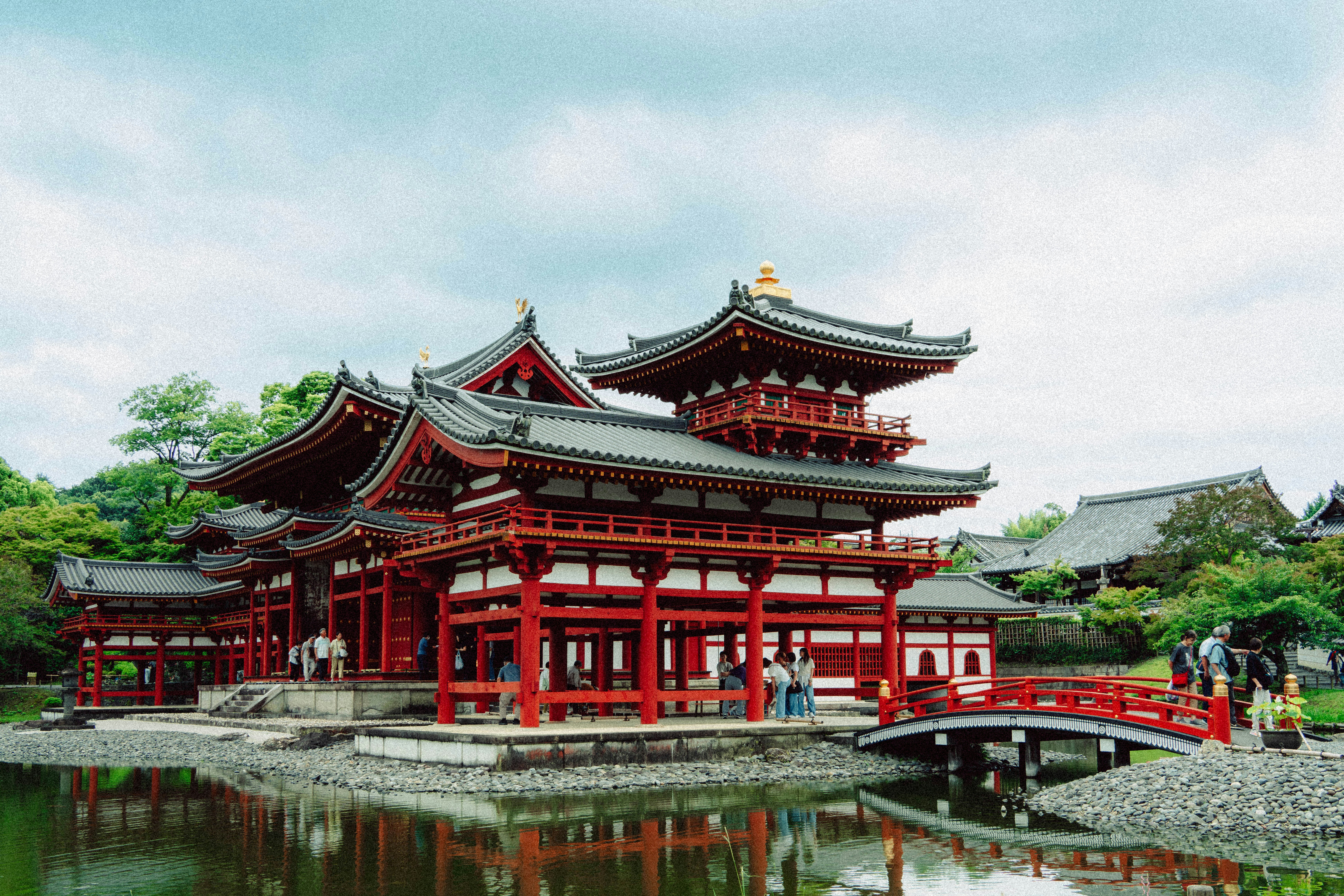 Historic japanese temple with red pillars reflected in water.
