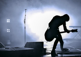 A guitarist performs on stage with dramatic backlighting and smoke.
