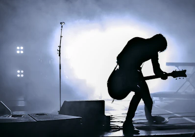 A guitarist performs on stage with dramatic backlighting and smoke.