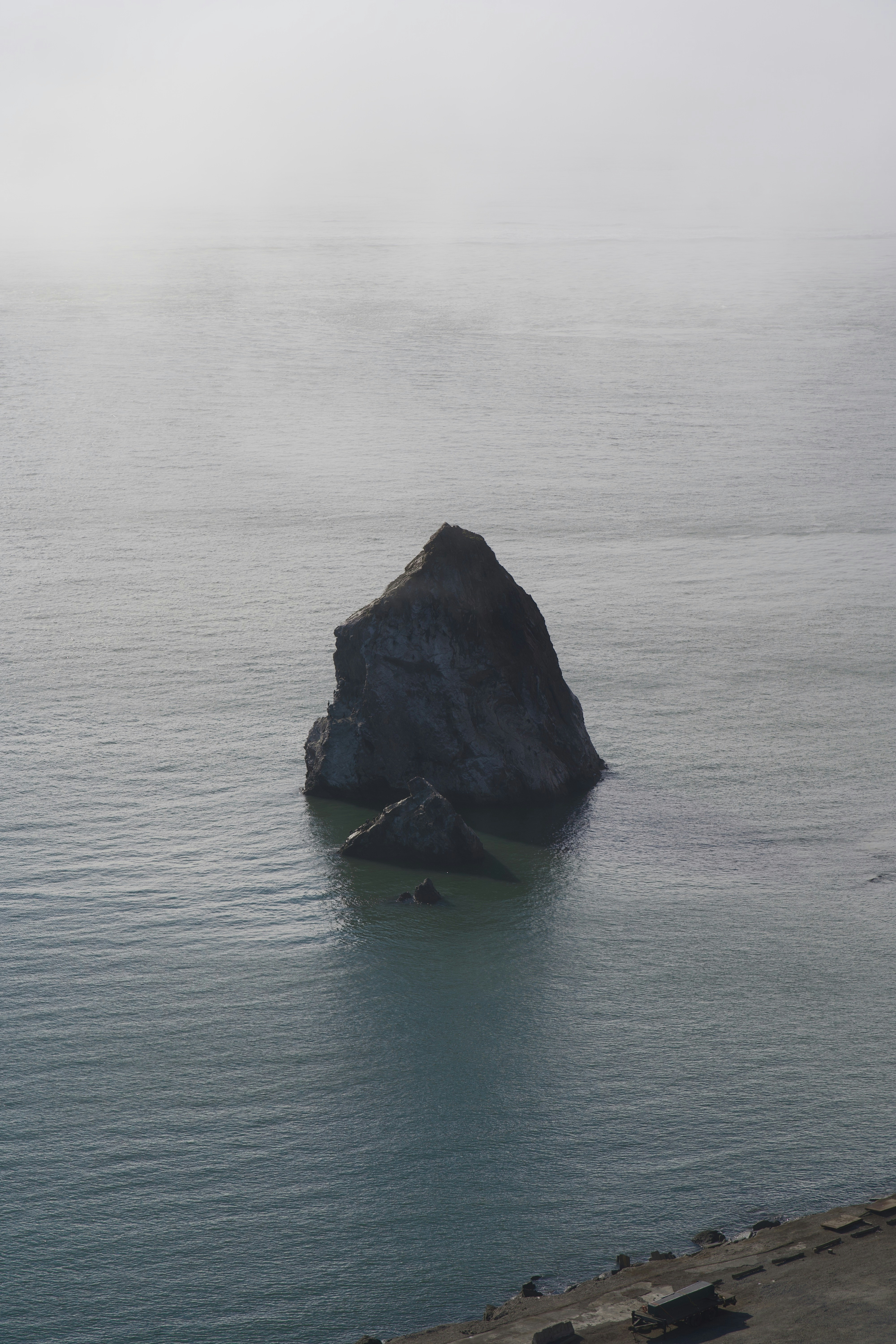 Una grande guglia rocciosa si erge nell'acqua calma e nebbiosa dell'oceano.