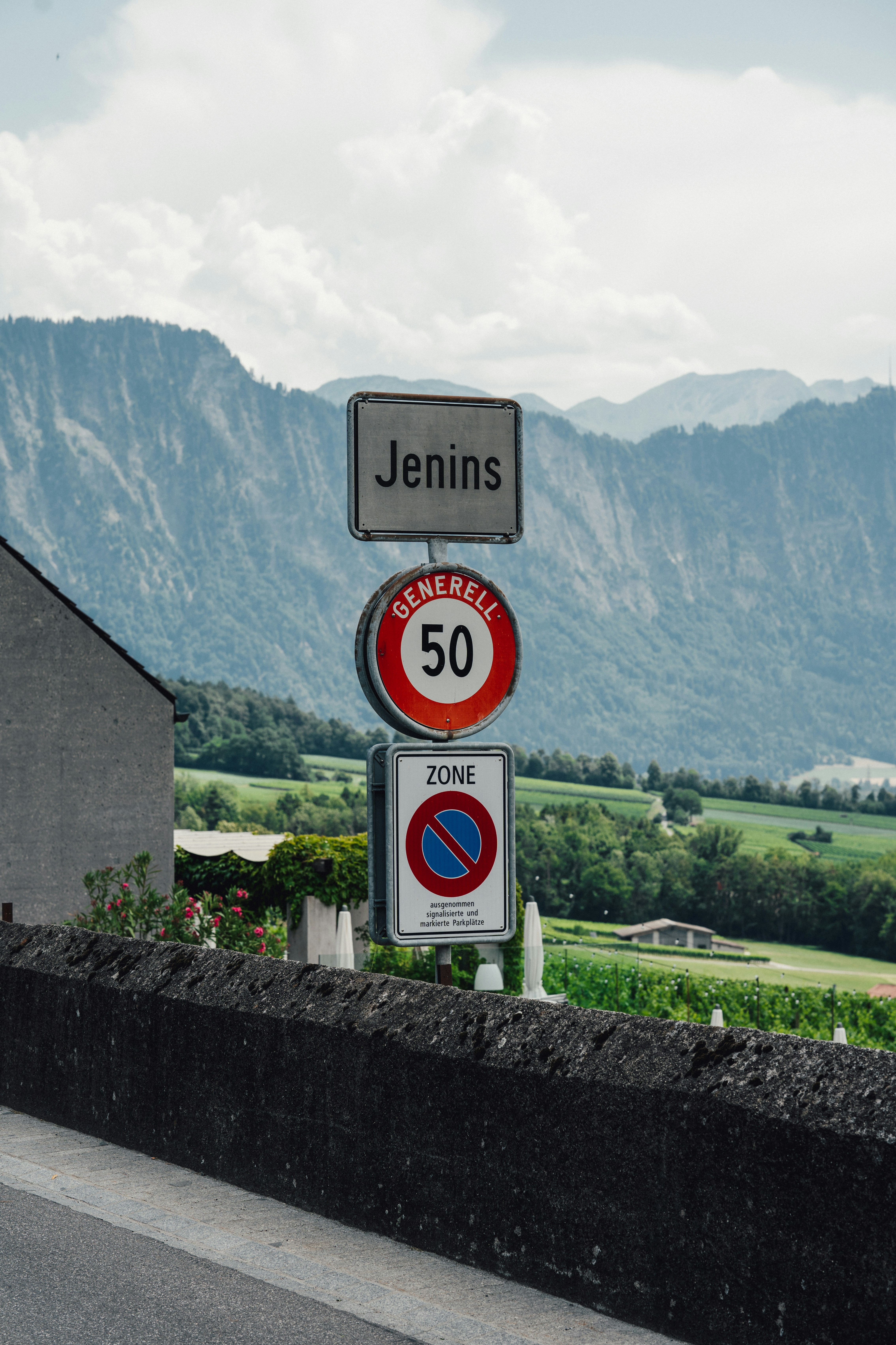 Jenins road signs against a mountainous, green landscape.