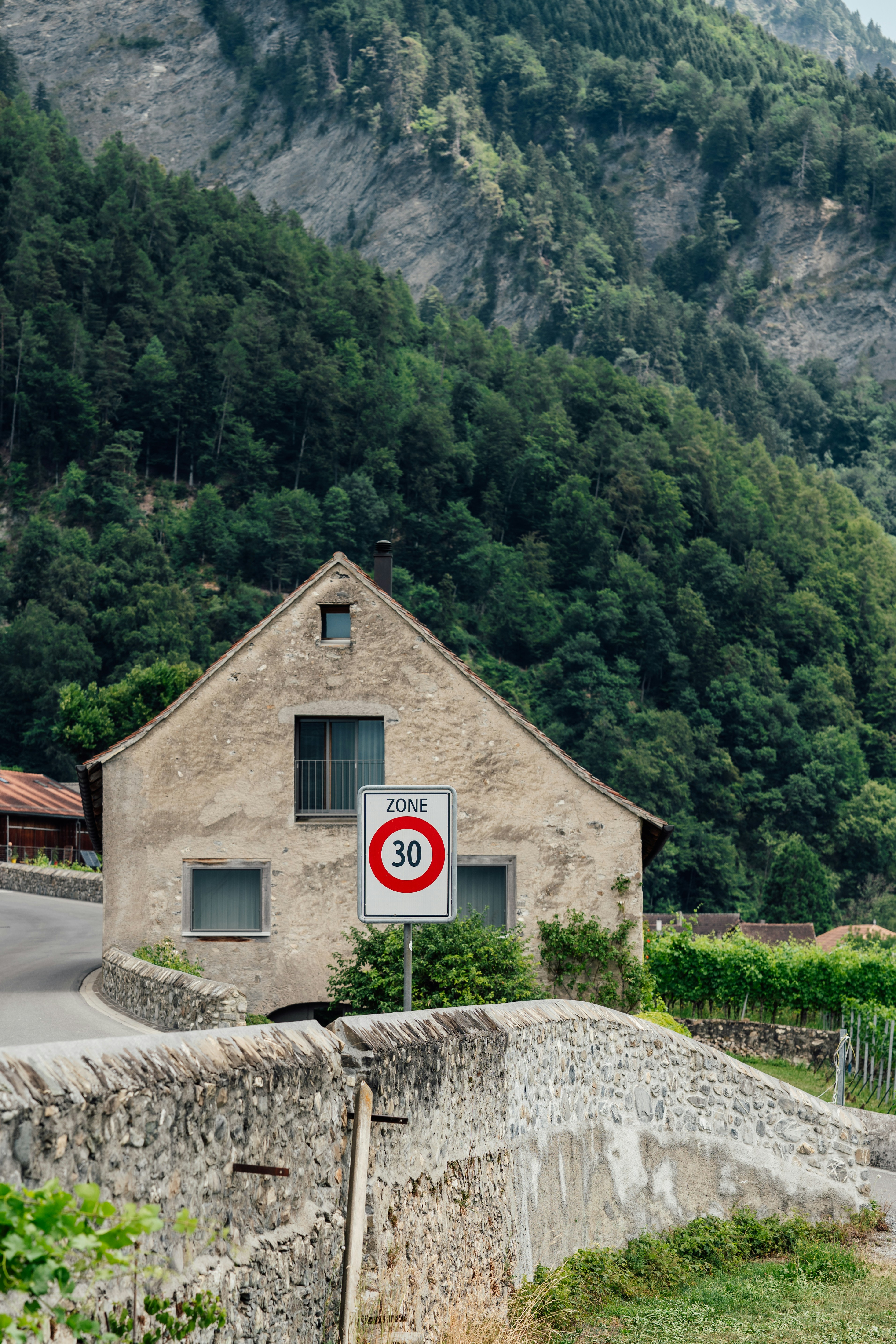 Old house, speed limit sign, stone bridge, and green mountain.