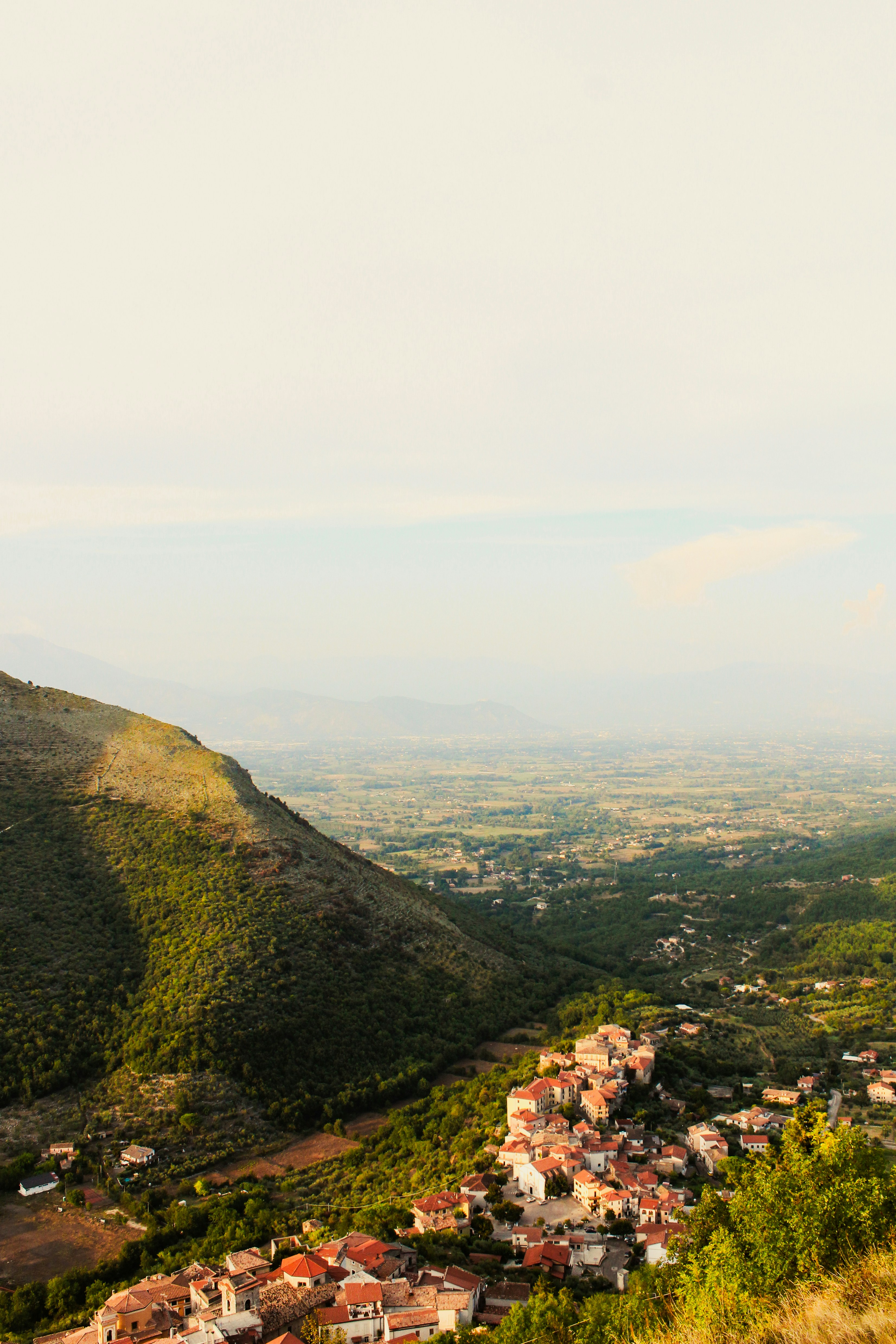 Village in a lush valley beside a large green mountain.