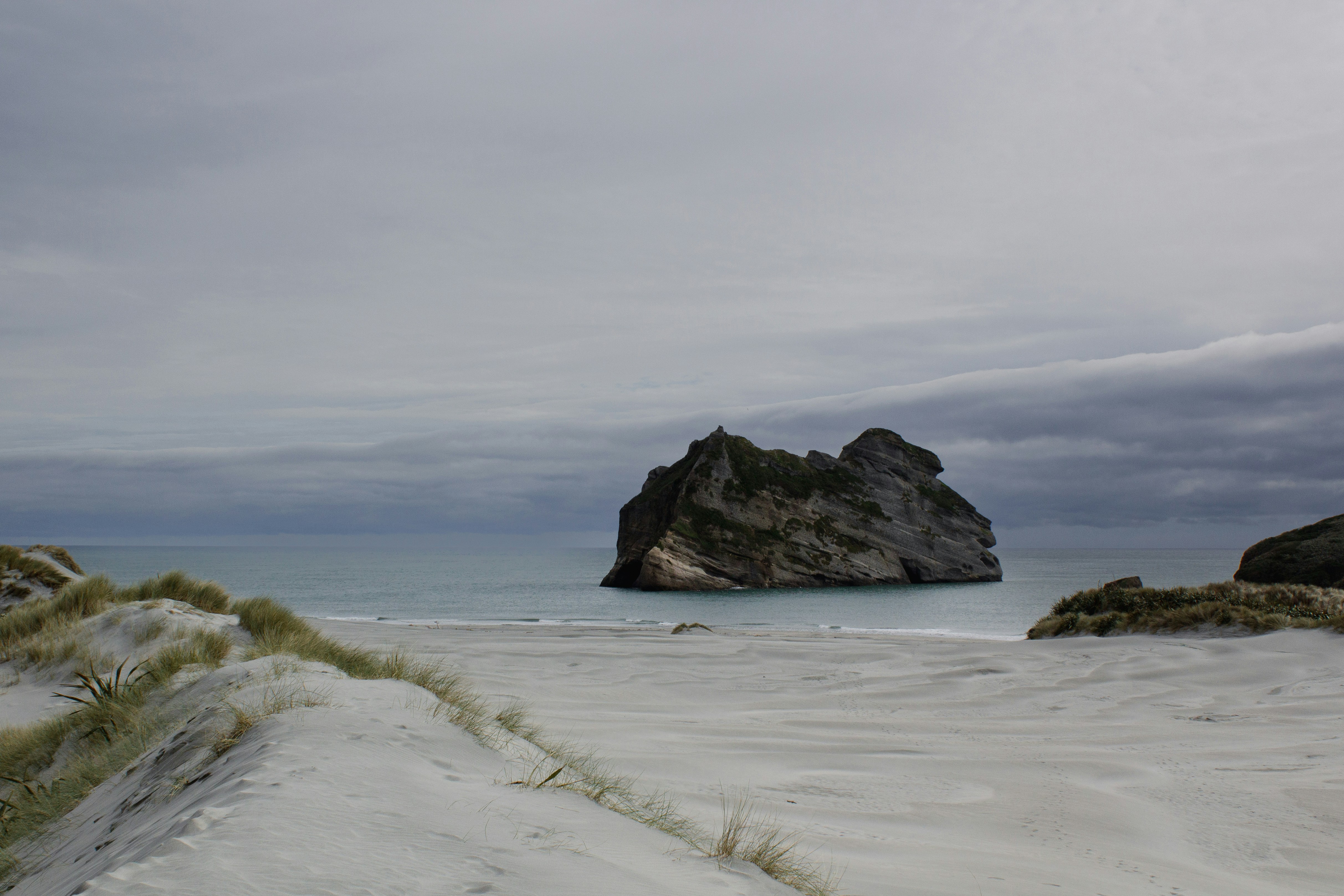 Sandy beach and a rocky island under a cloudy sky.