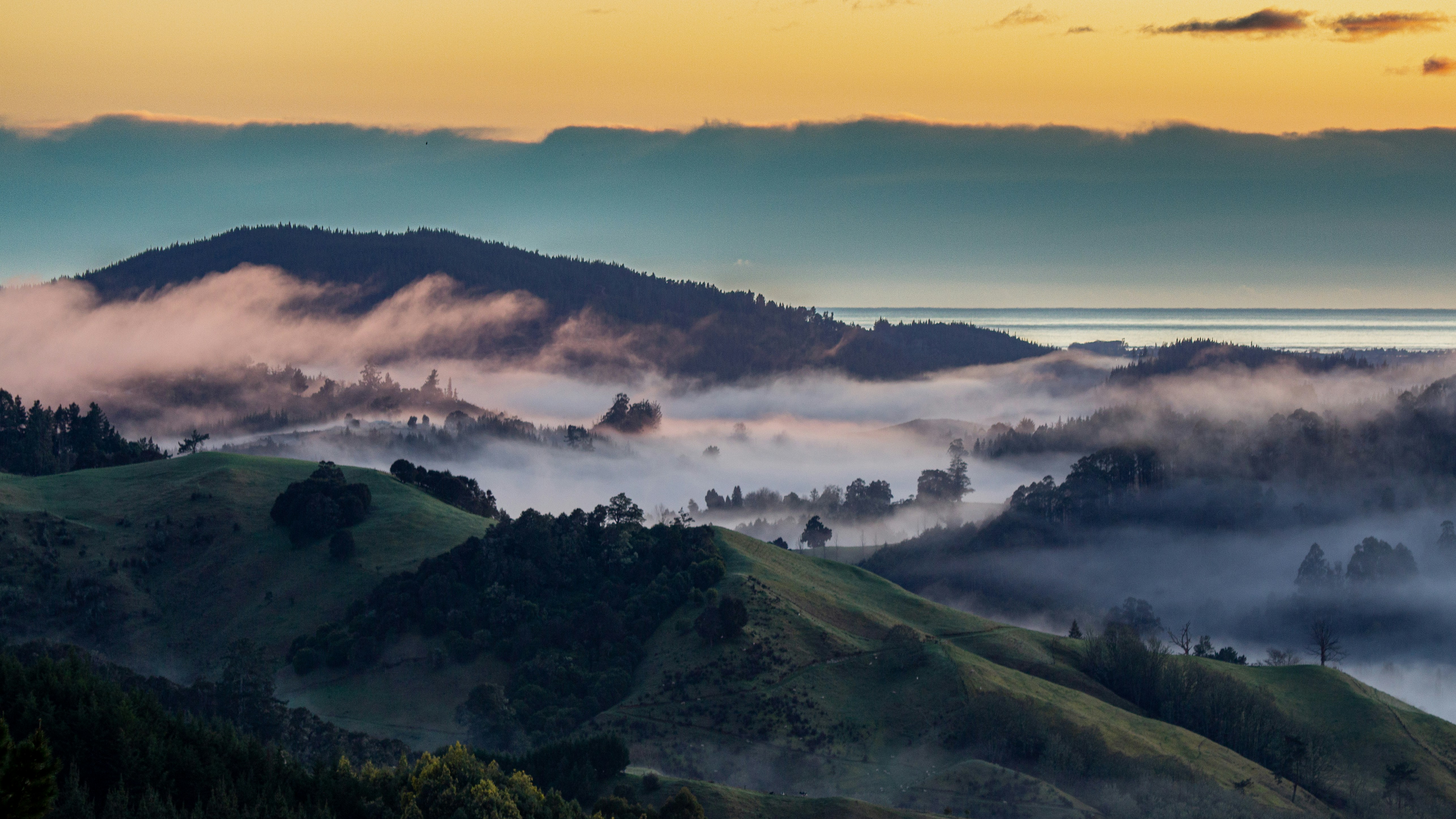 Foggy mountains at sunrise with ocean in the background.