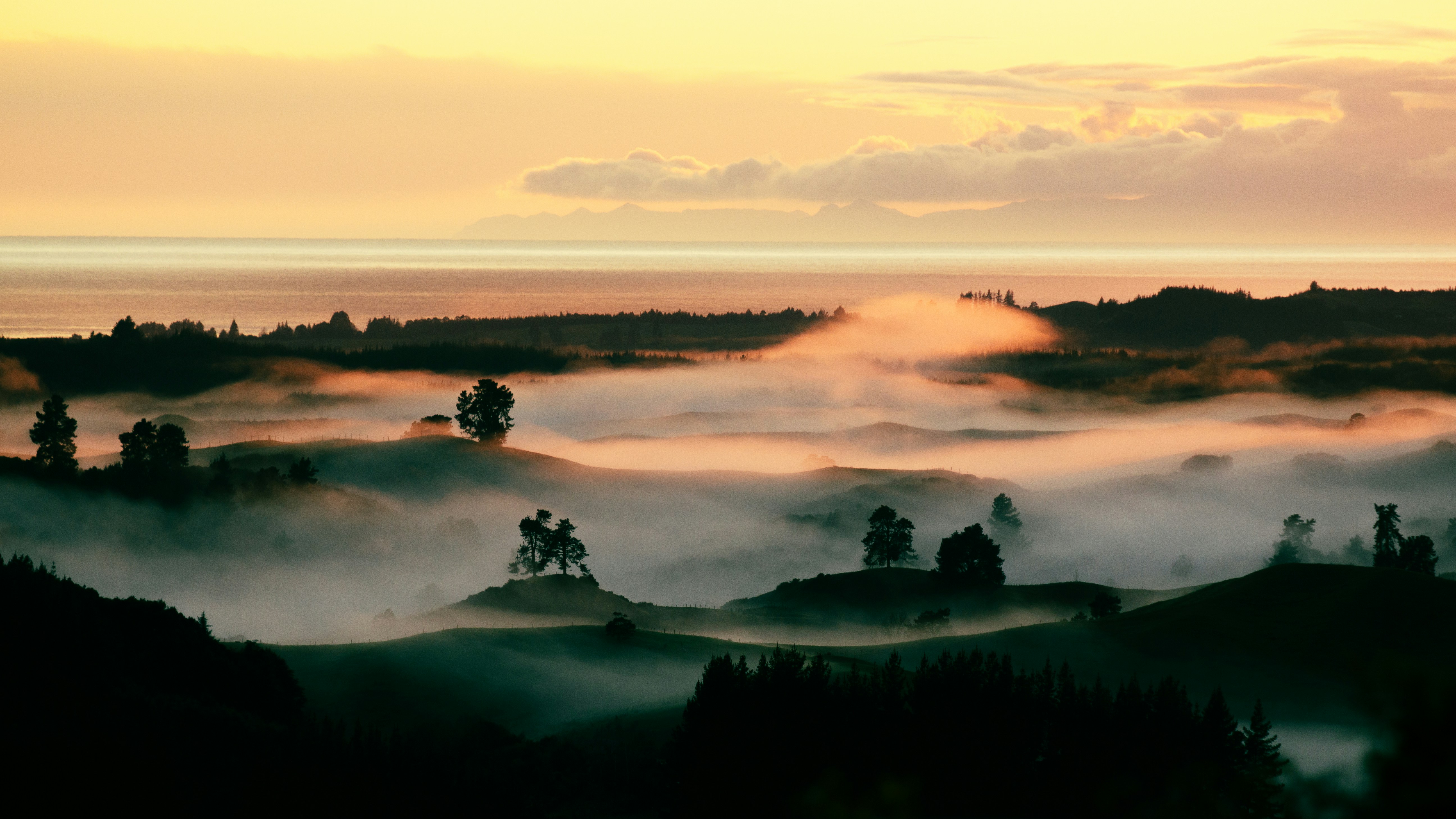 Golden sunrise over misty hills and distant ocean.