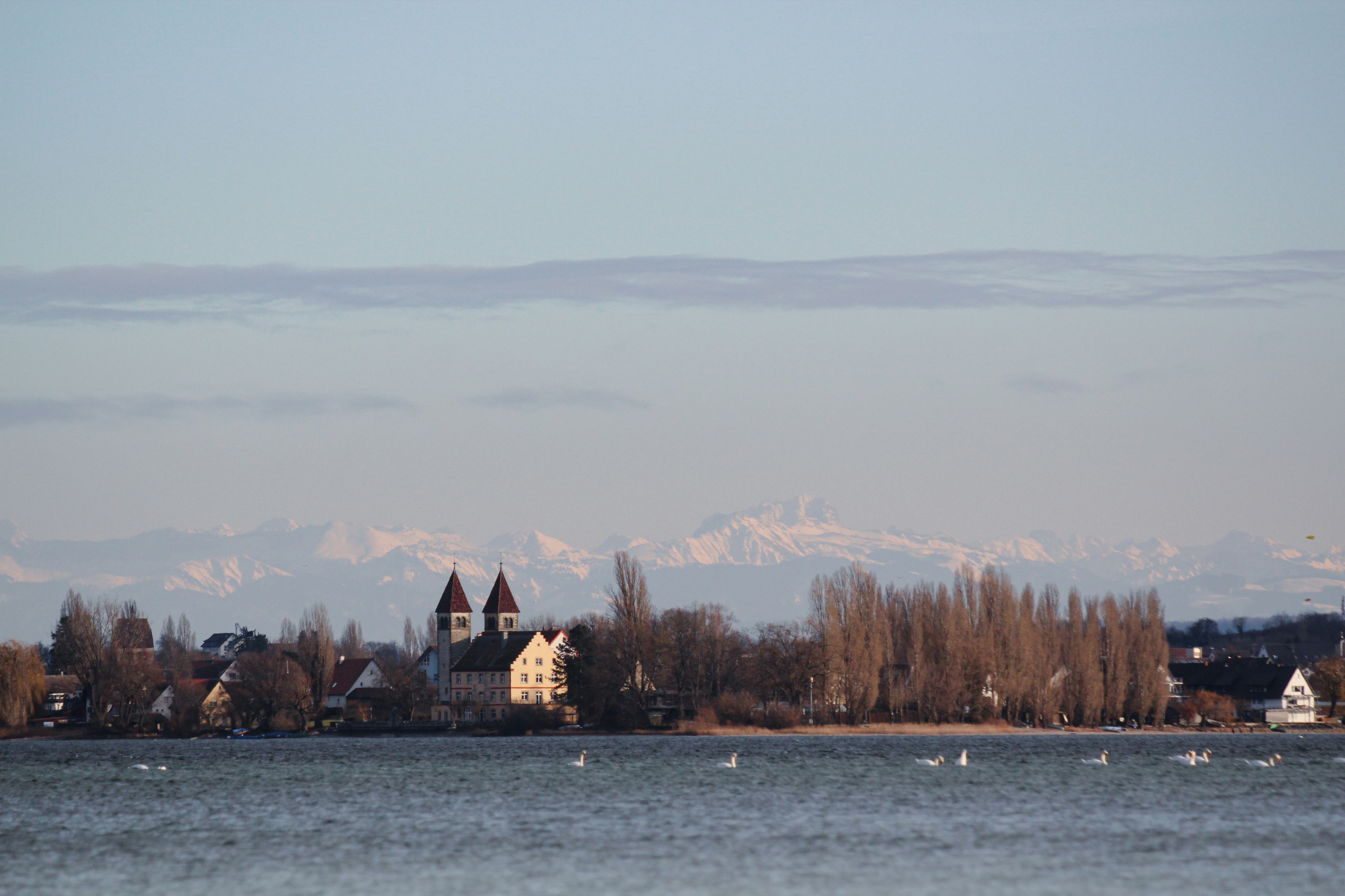 Lakeside town with church and distant snow-capped mountains.