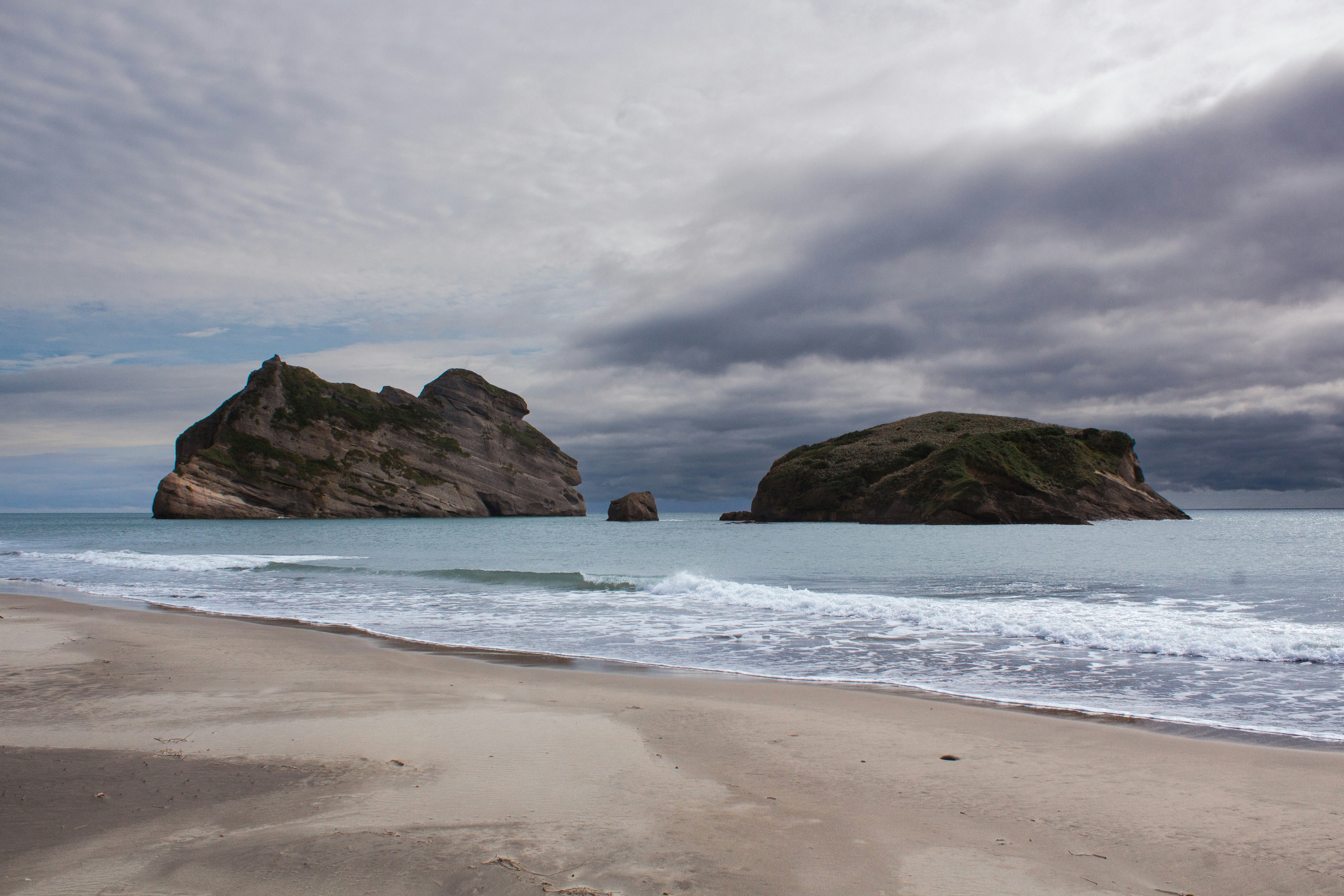 Rocky islands in ocean with sandy beach and cloudy sky.