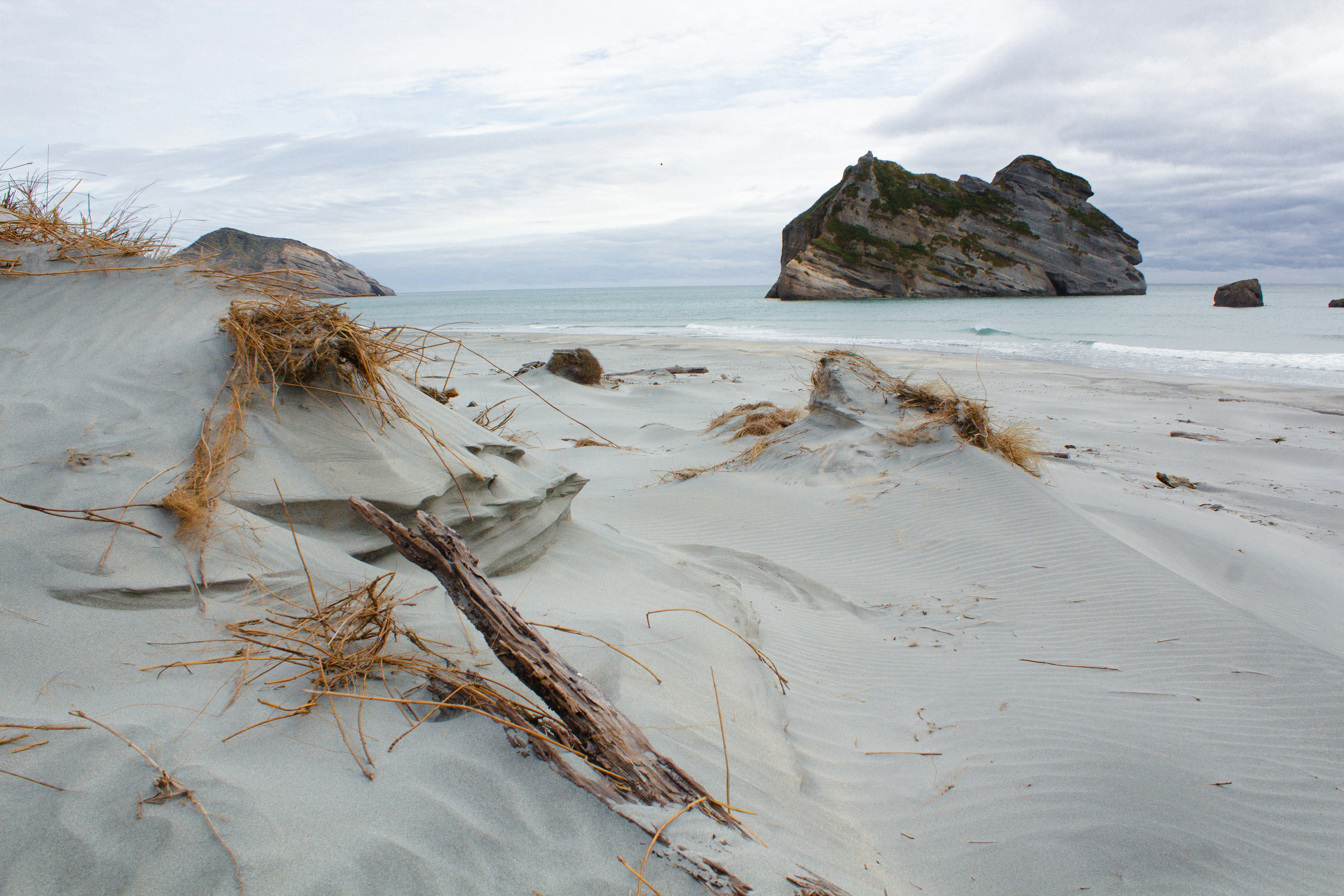 Rocky islands offshore from a sandy beach with dunes.