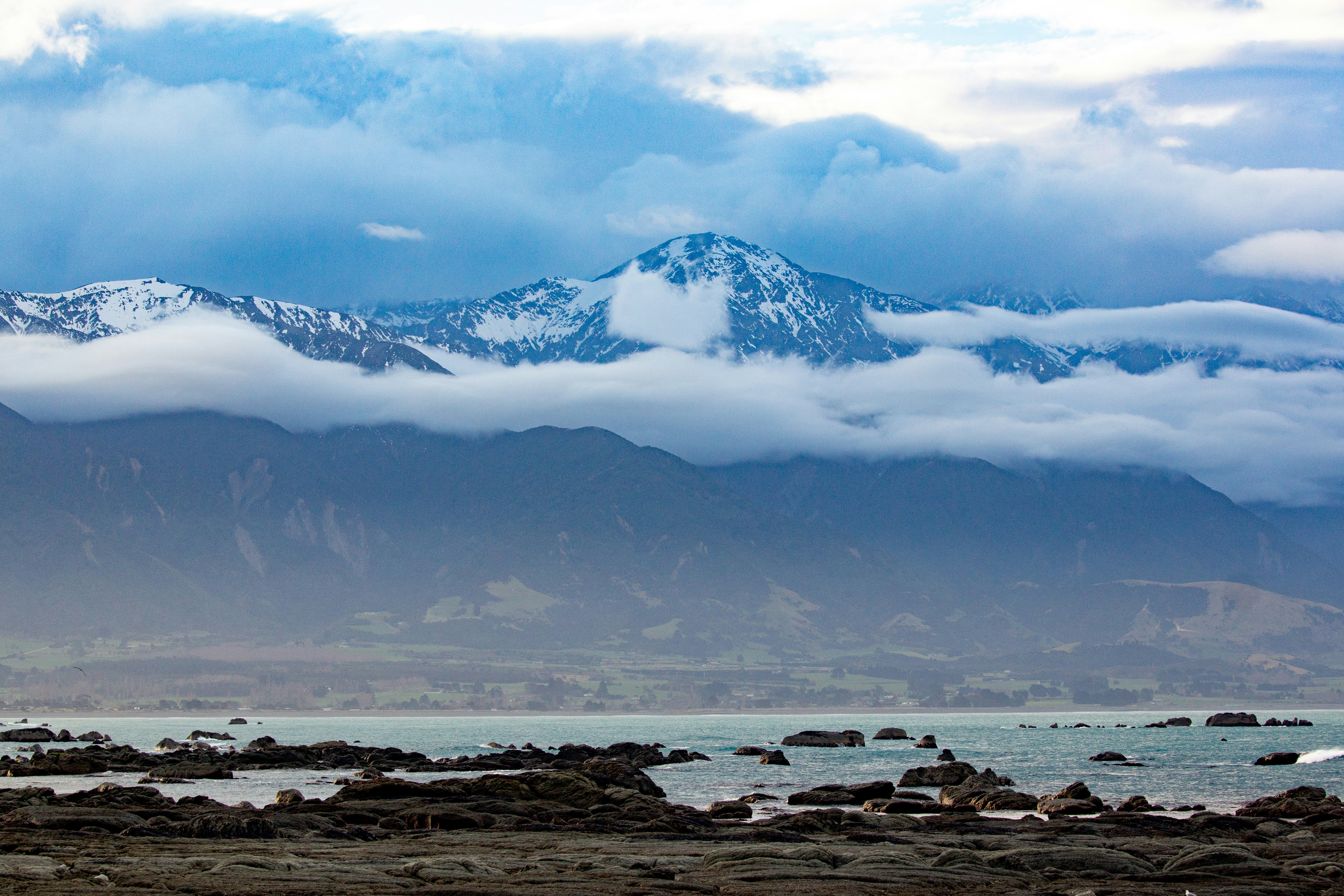 Snowy mountains shrouded in clouds over a rocky coastline.