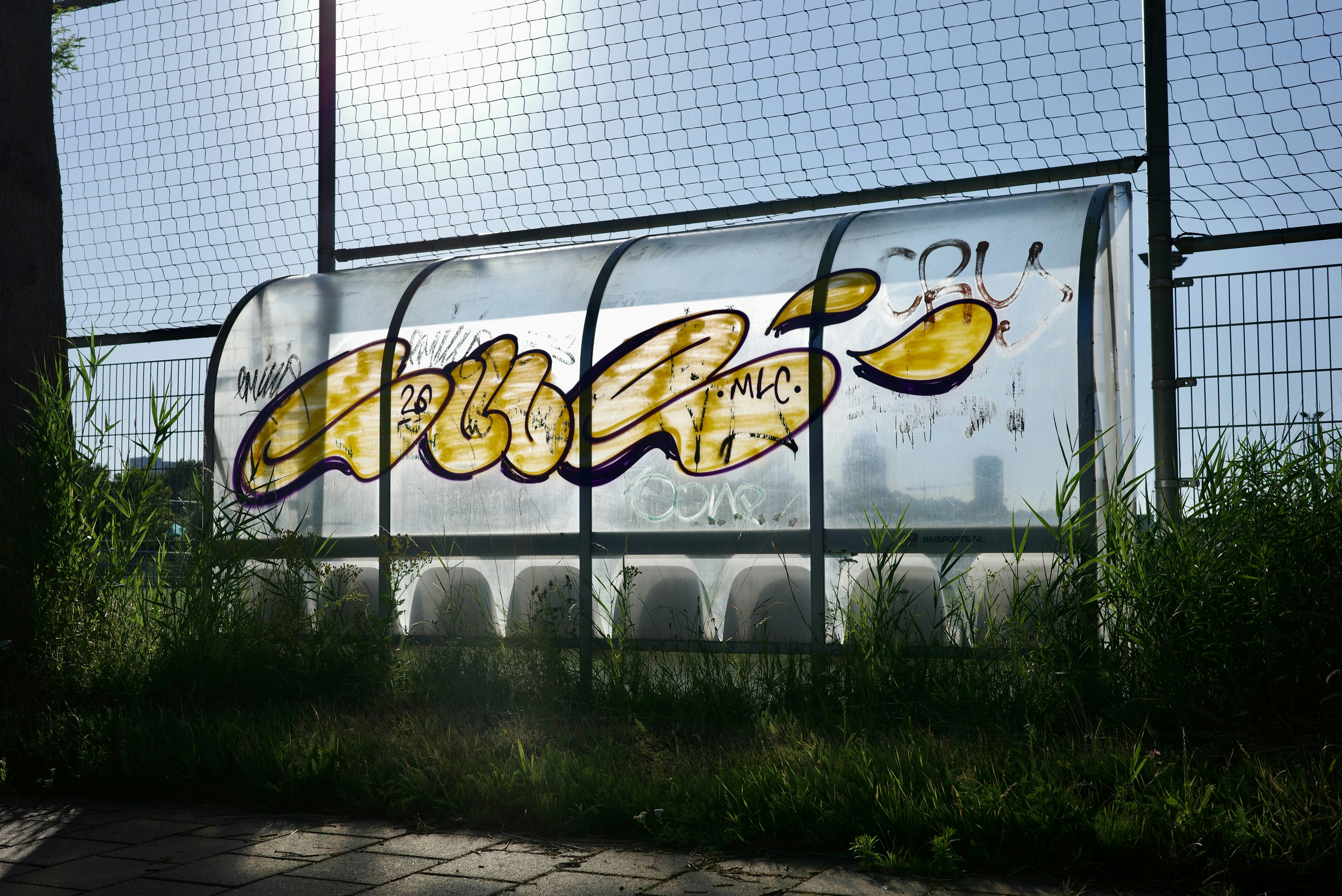 Outdoor transparent shelter with yellow graffiti and seats