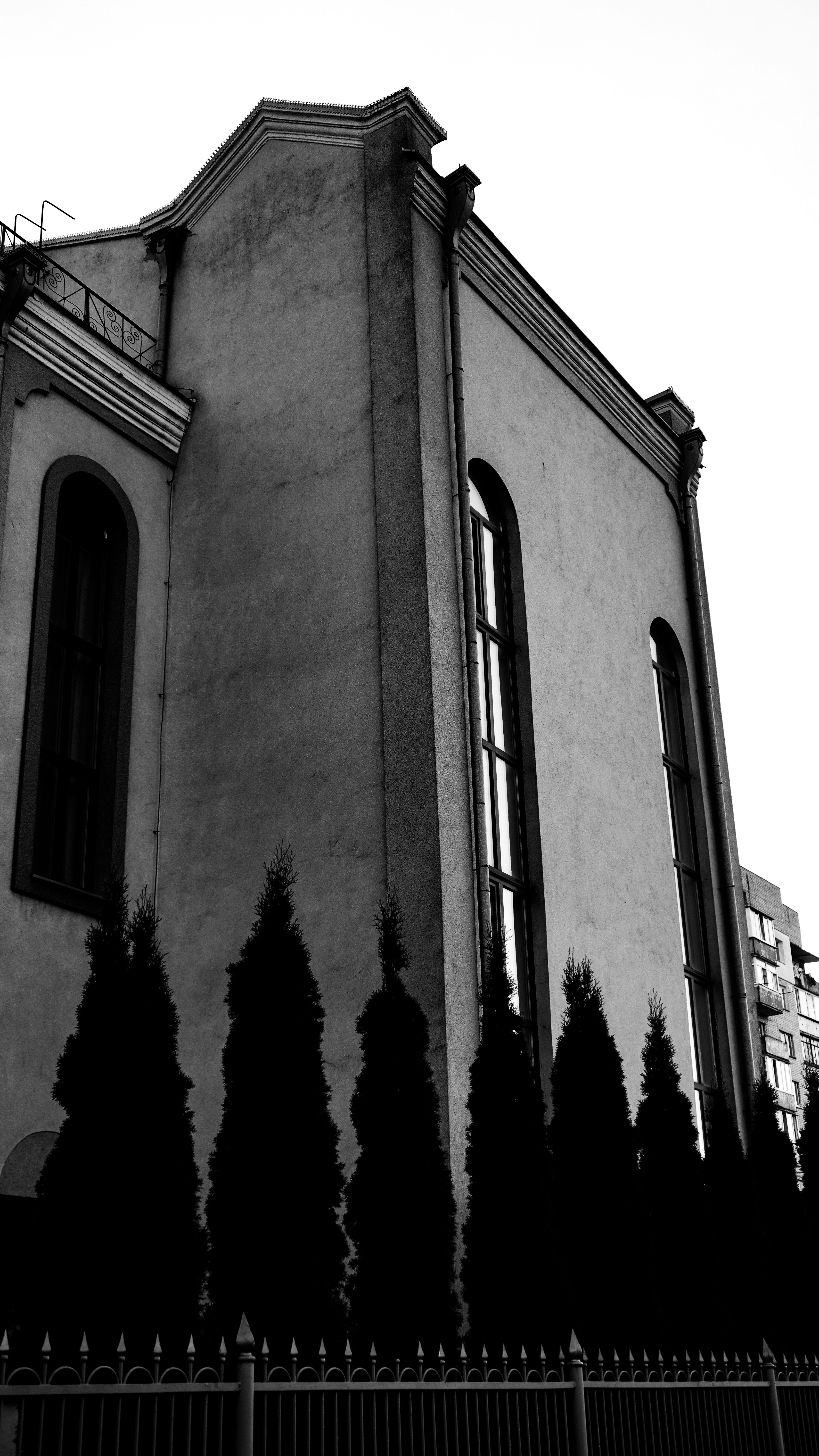 Facciata monocromatica dell'edificio con finestre ad arco e alberi in controsagoma.
