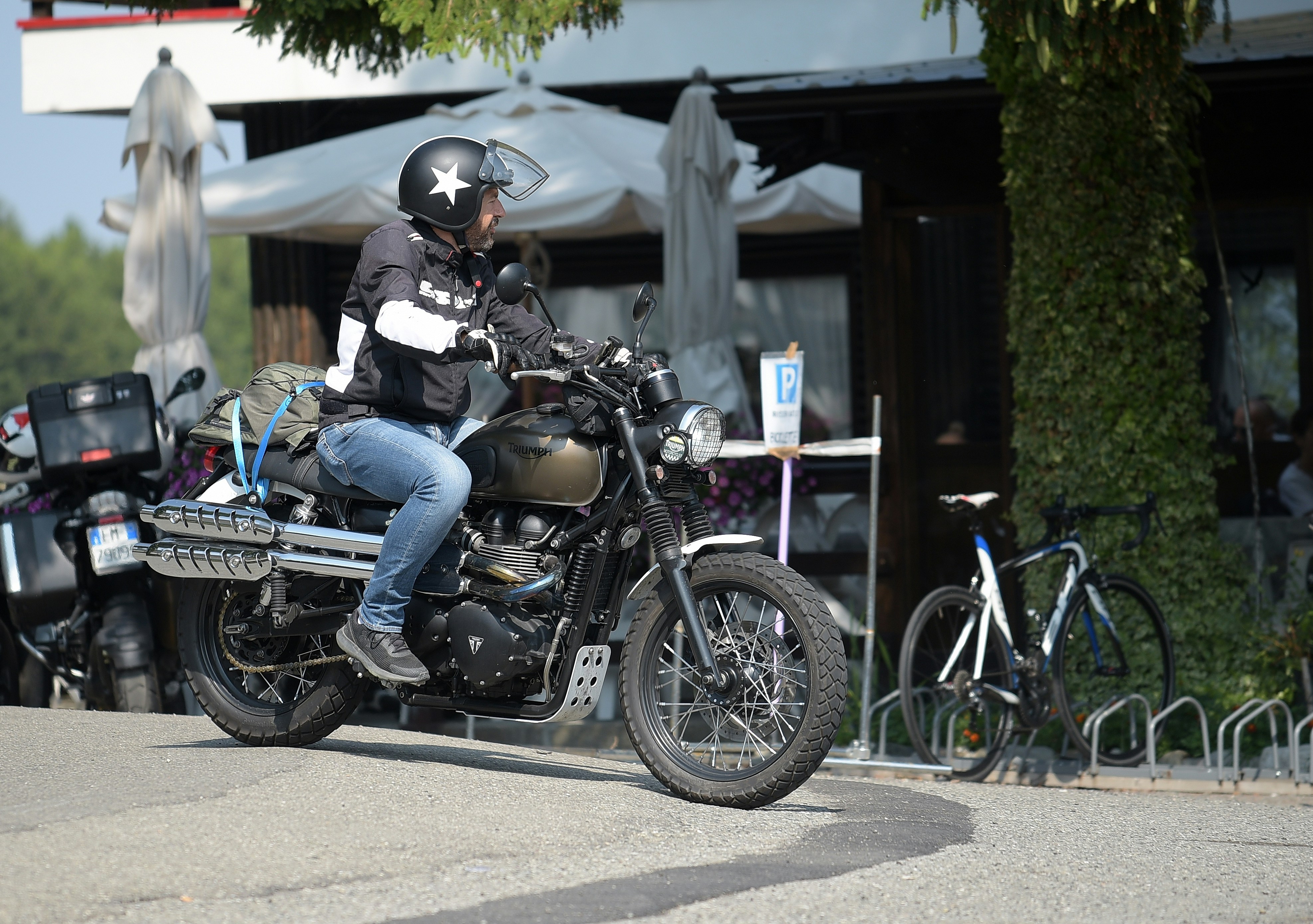 Person riding a motorcycle with gear past an outdoor cafe.