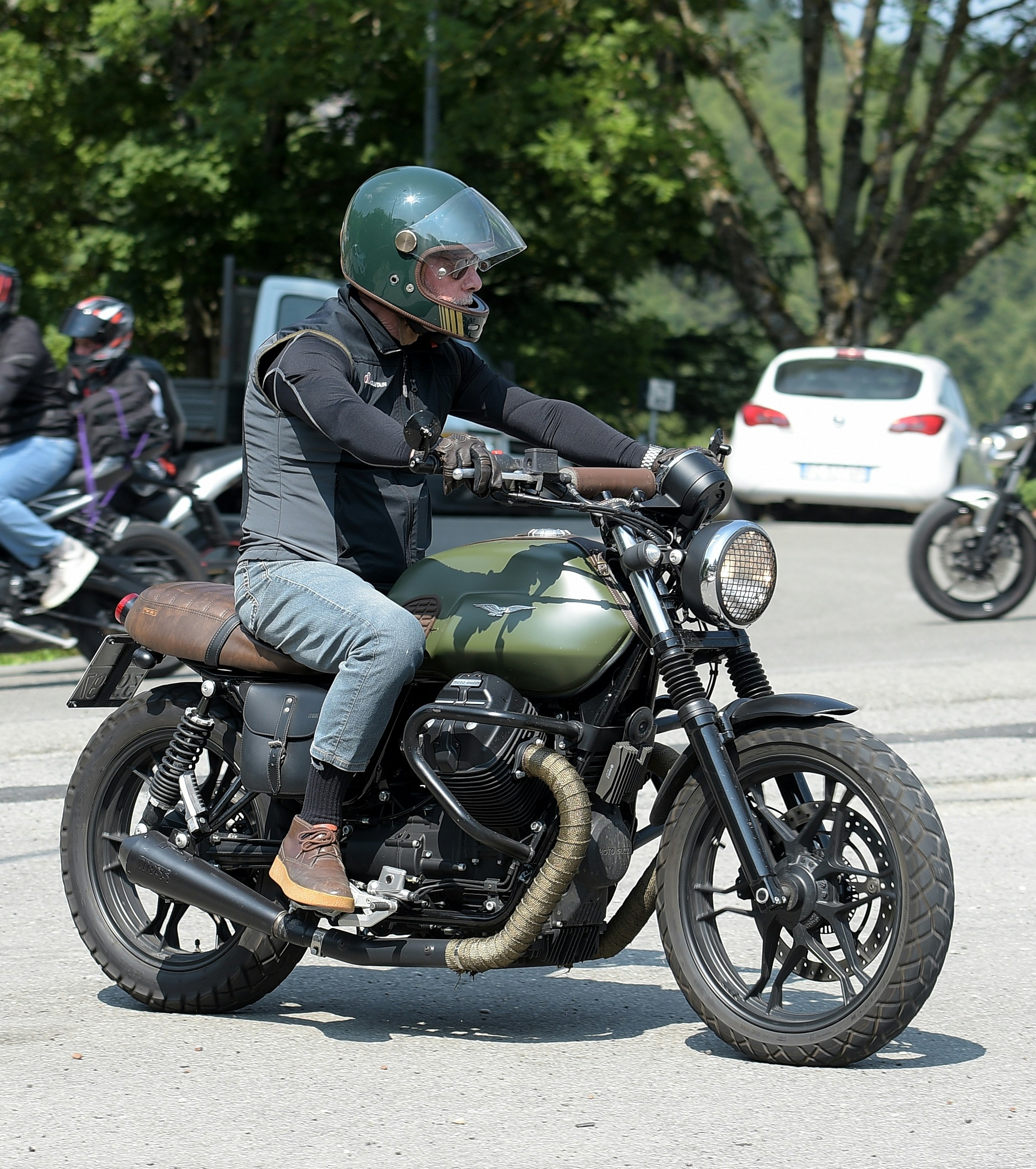 Man in helmet riding a green custom motorcycle outdoors.