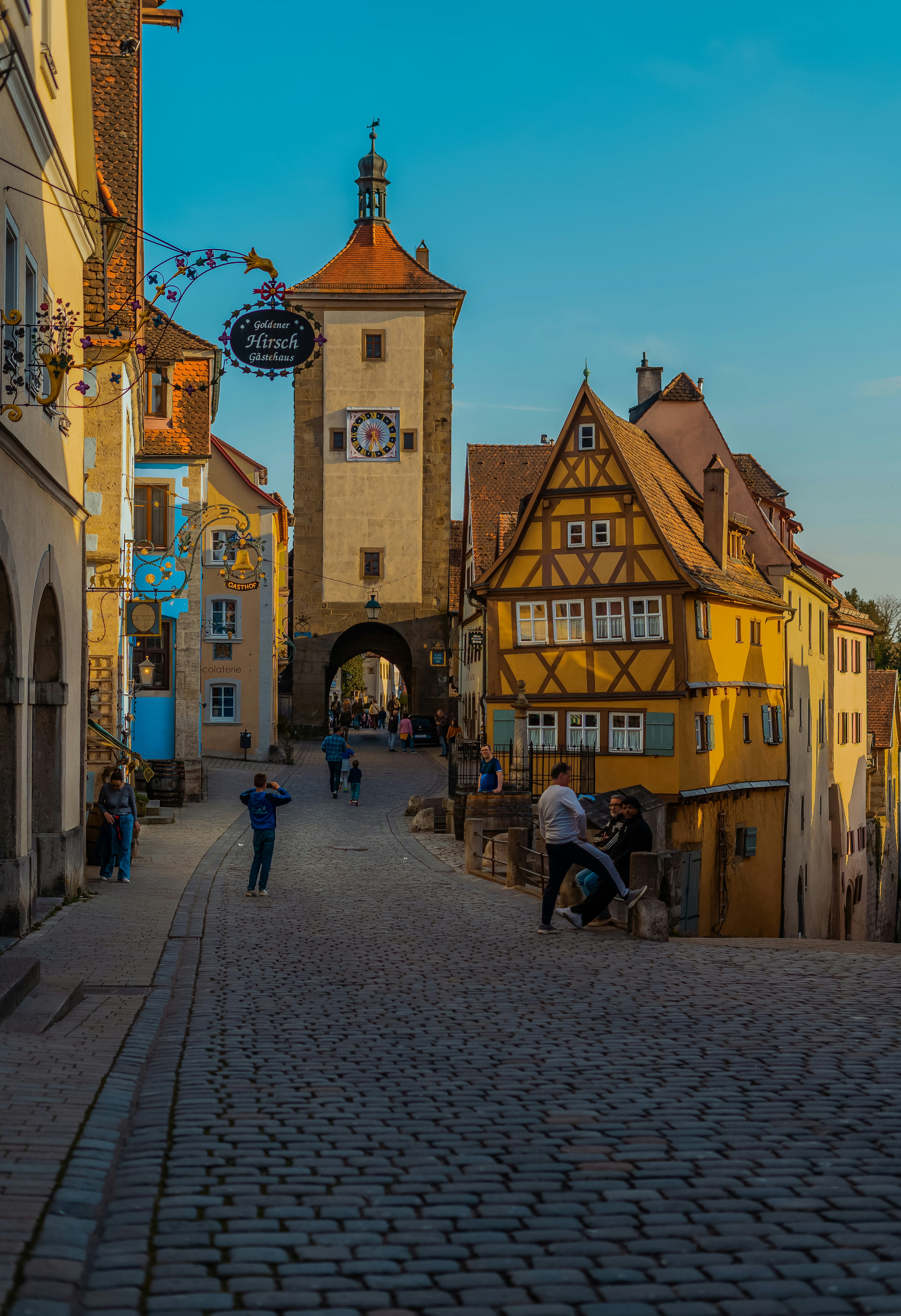 Rua histórica europeia com torre do relógio e edifícios coloridos.