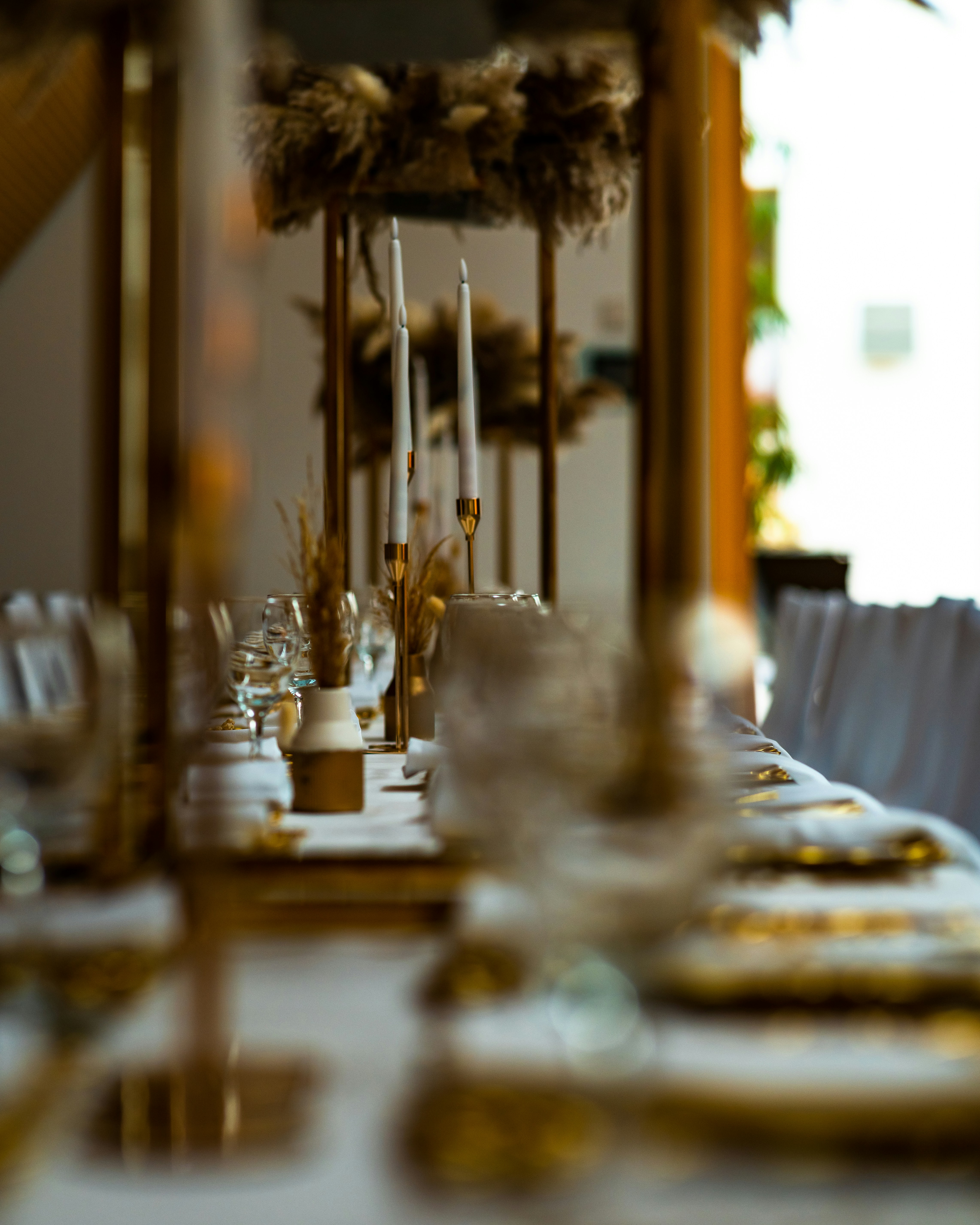 Mesa longa elegante, decorada em dourados e velas brancas.
