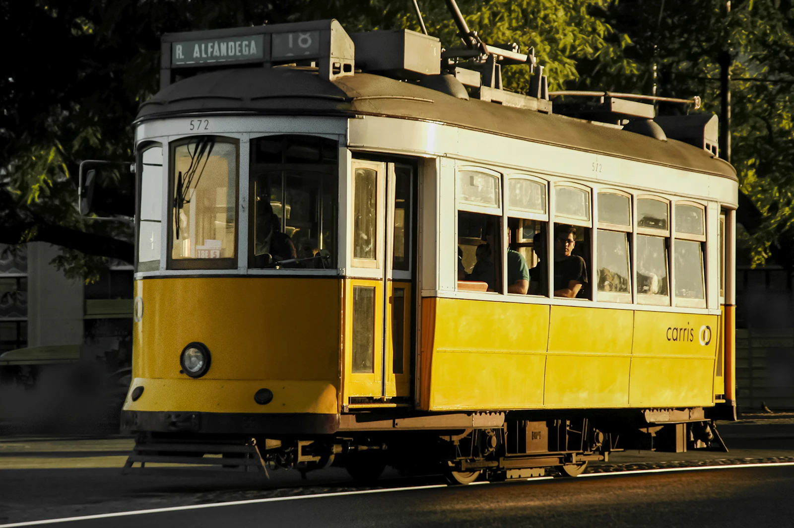 A classic yellow tram travels through a sunlit street in Lisbon