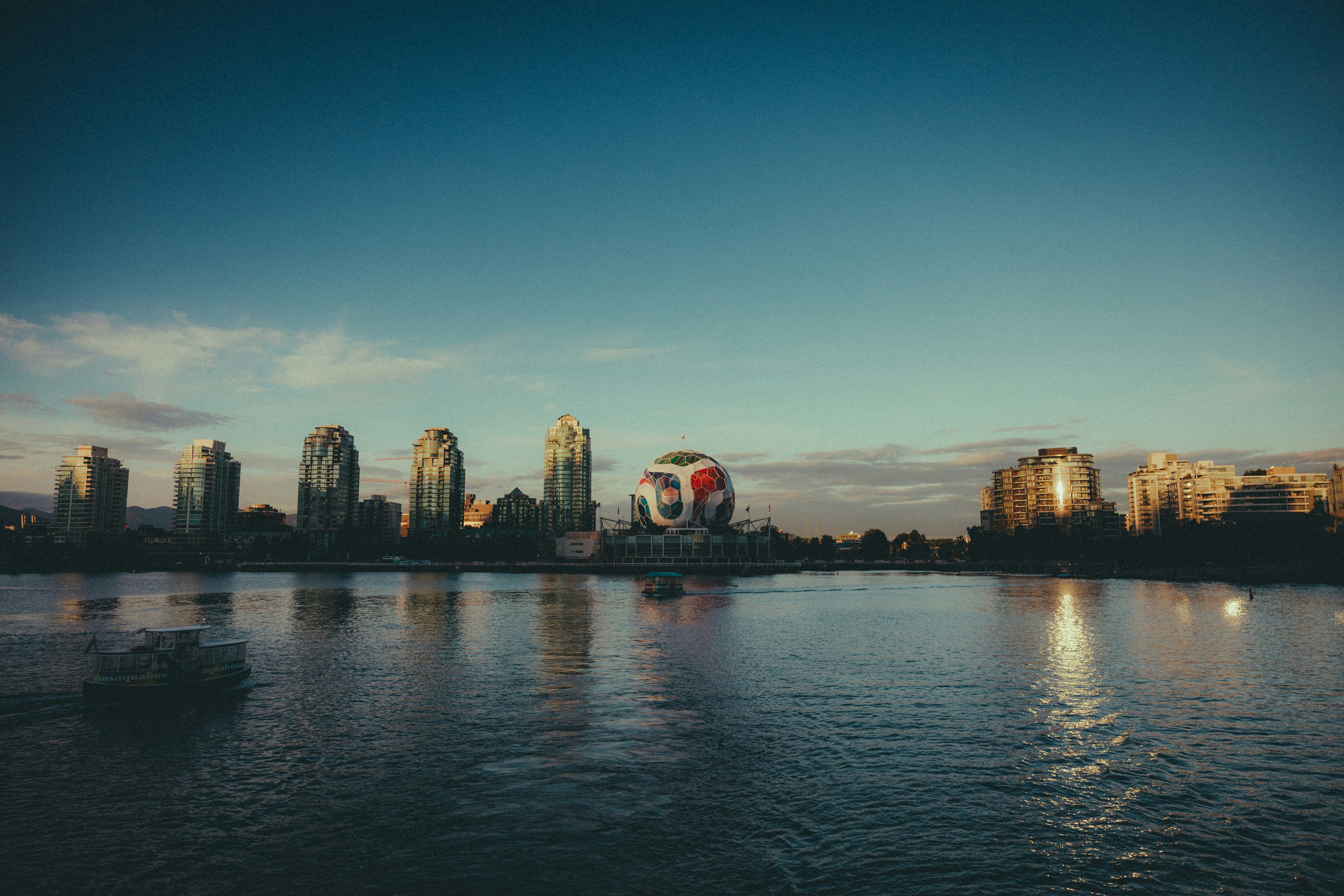 City skyline with spherical building across river under blue sky.