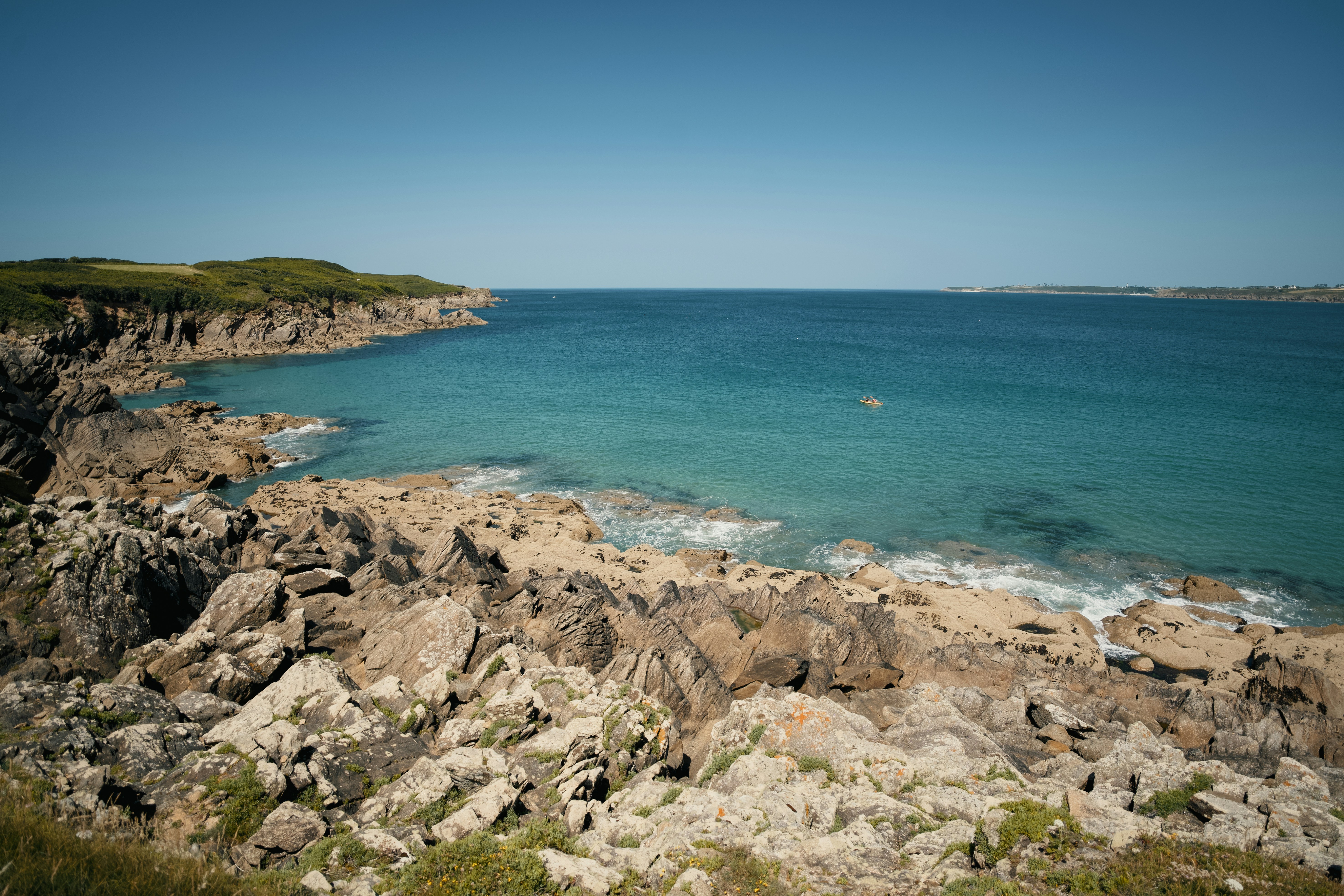 Rocky coastline with clear blue ocean under a bright sky.