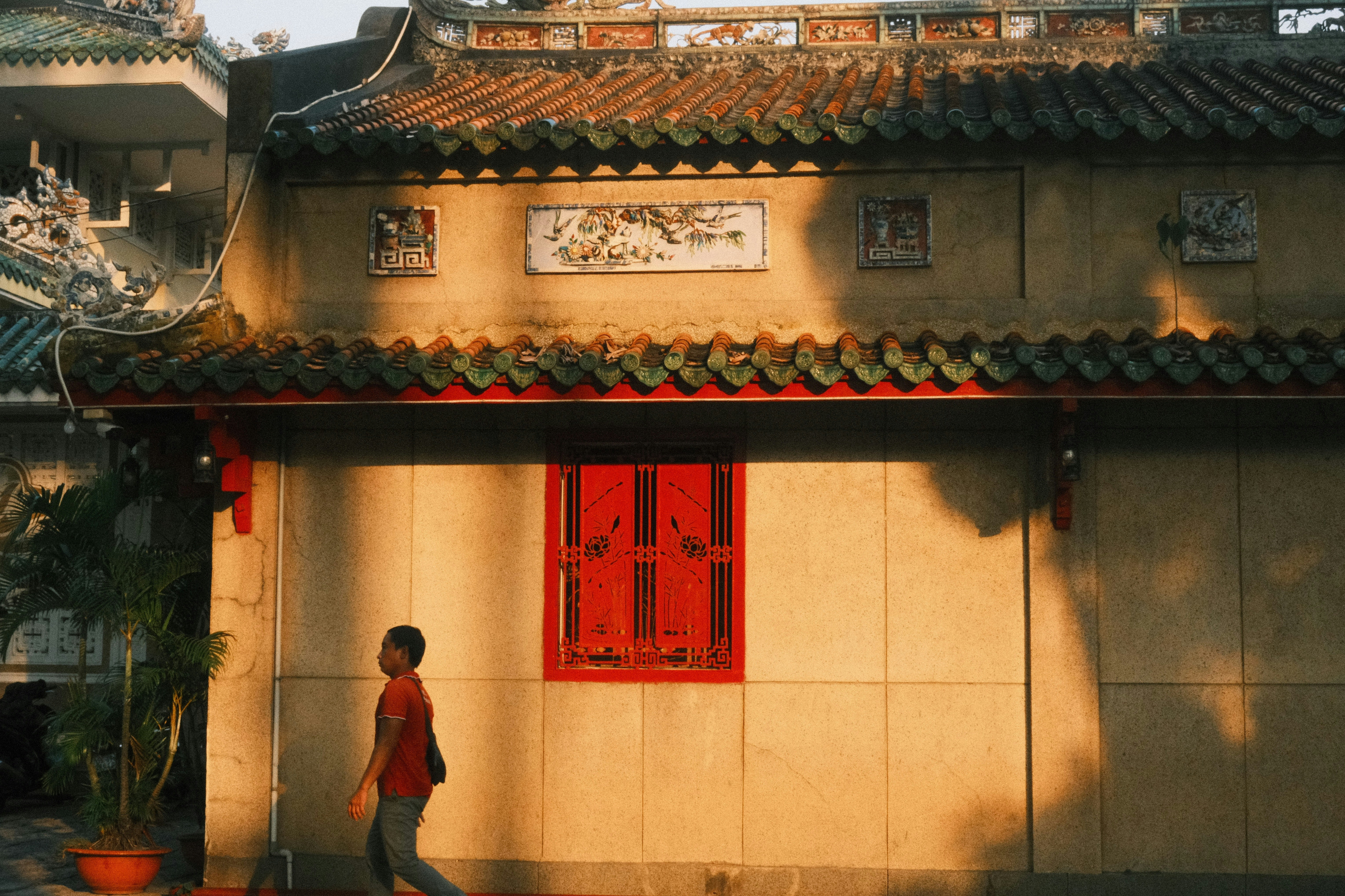 Golden light illuminates a person walking past a traditional building.