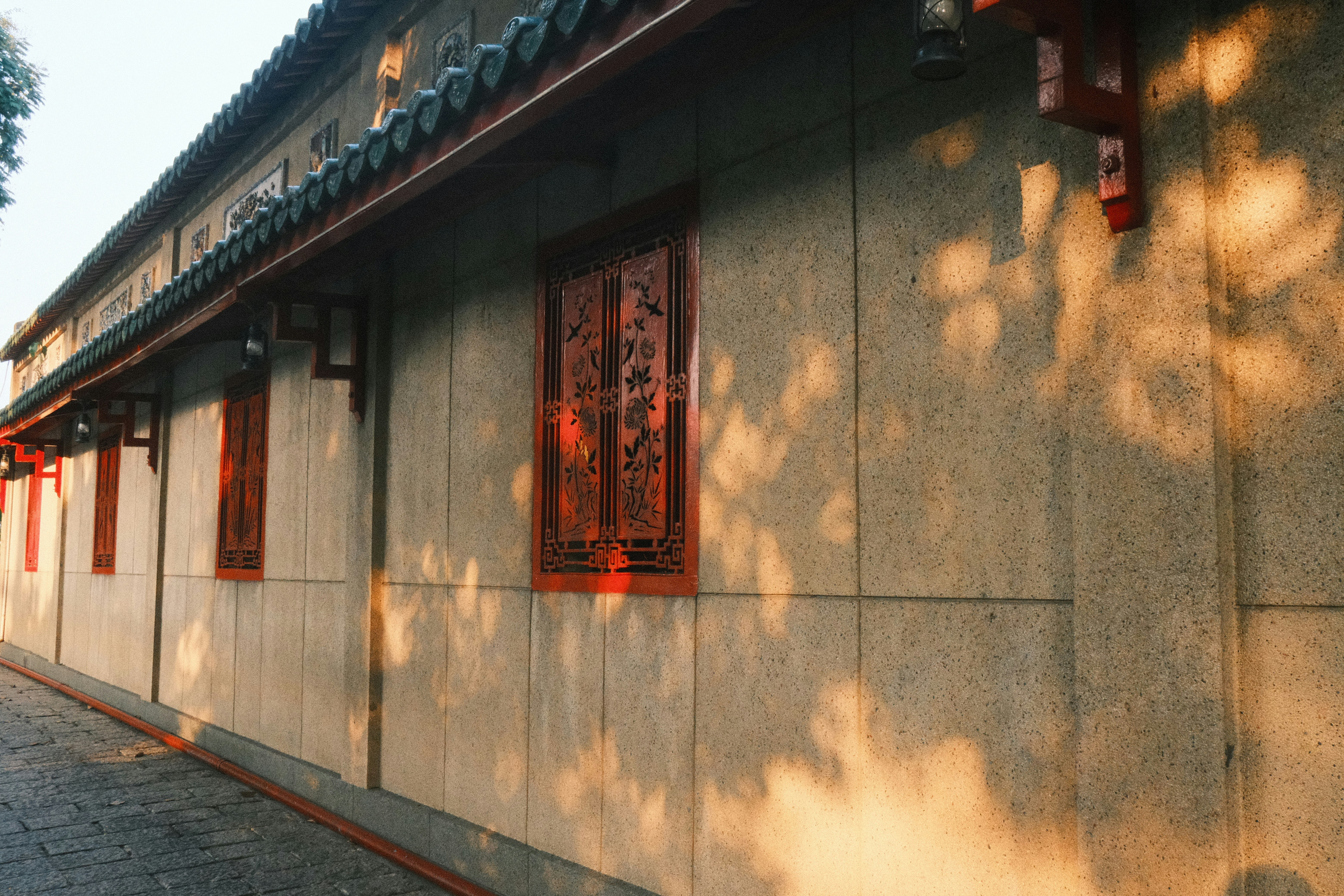 Traditional building wall with ornate red windows and tree shadows.