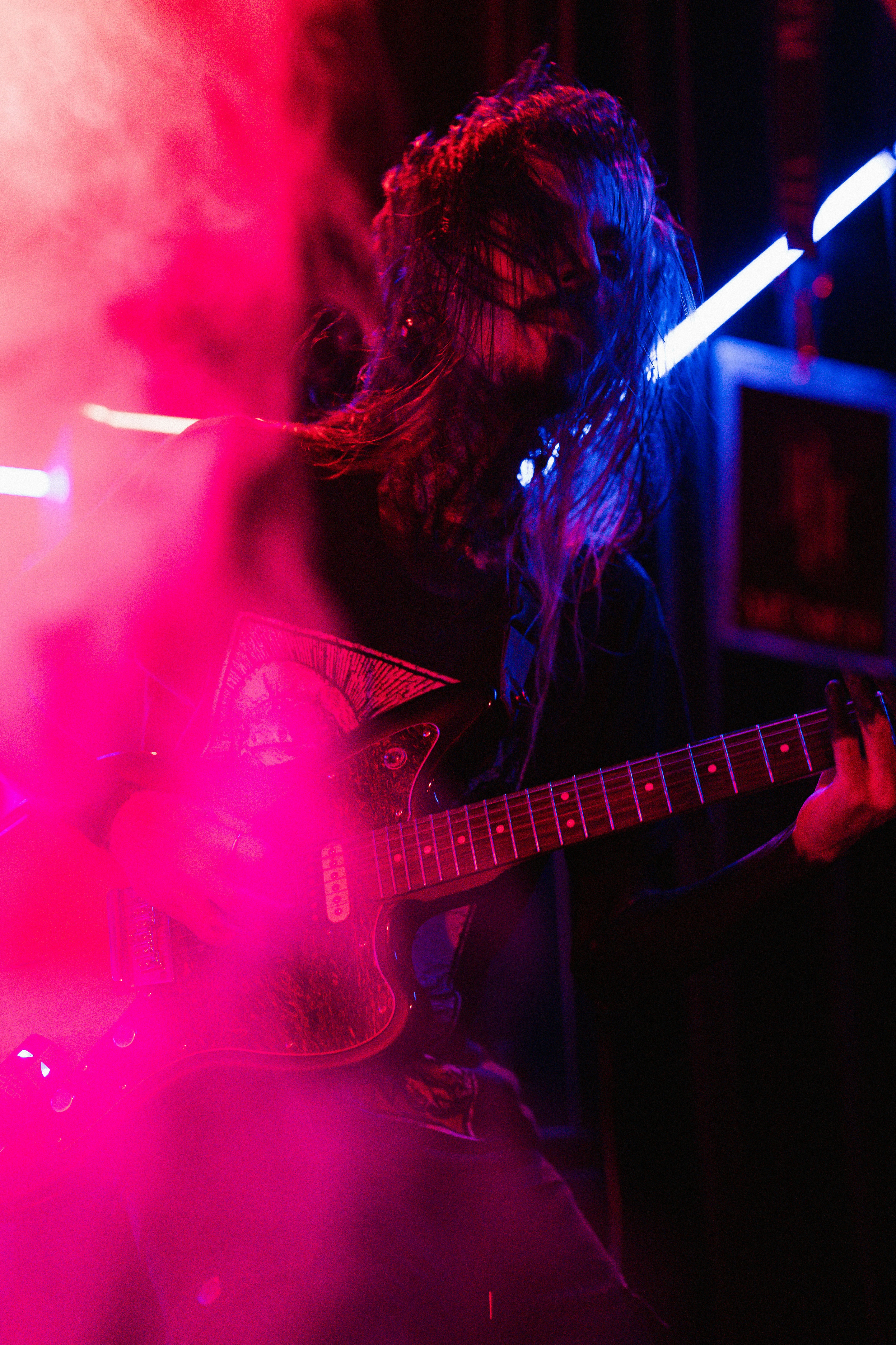 Pessoa tocando guitarra elétrica com iluminação vermelha e azul