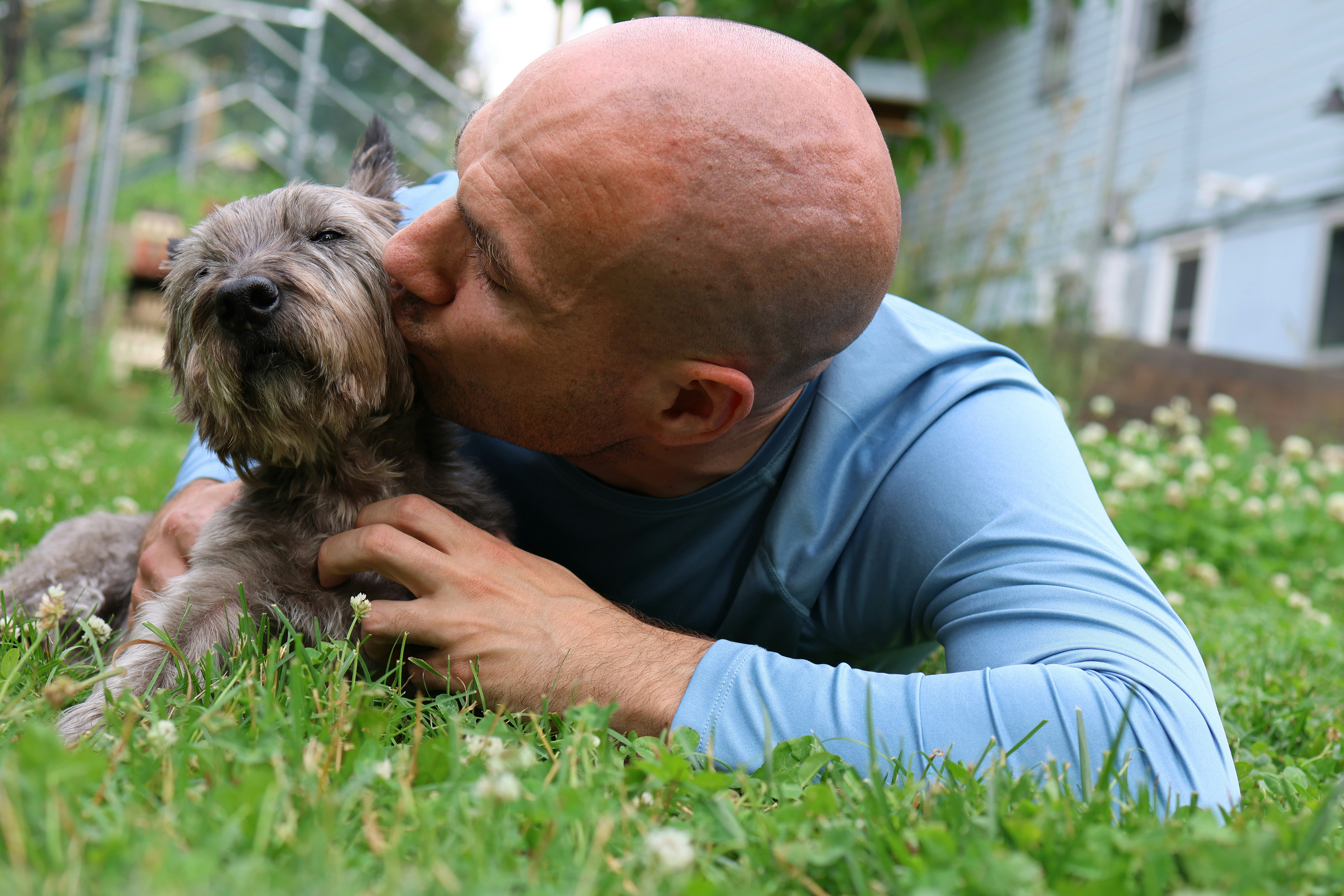 A man kisses his dog while lying in green grass.