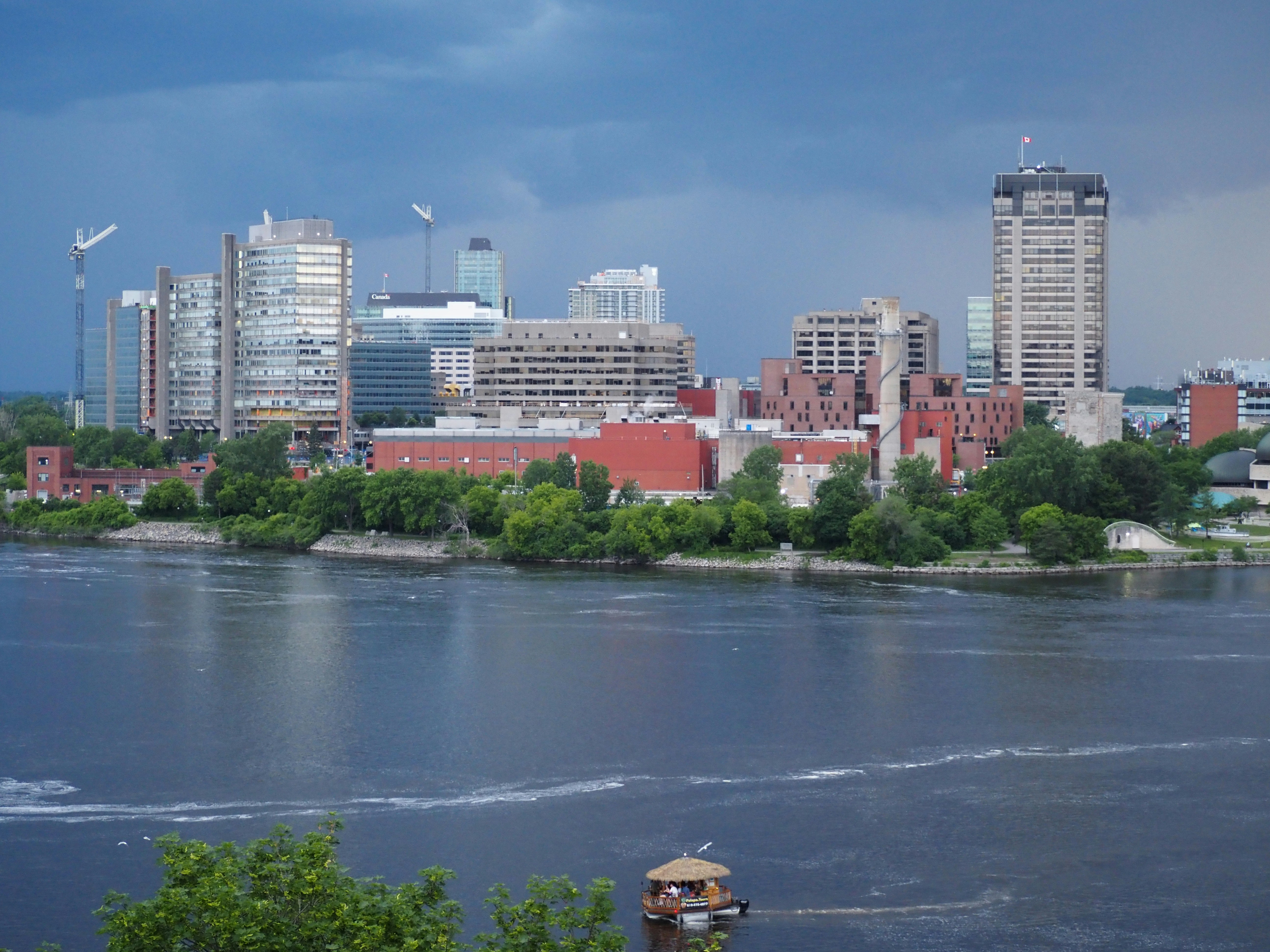 City skyline across a river under a dramatic cloudy sky.