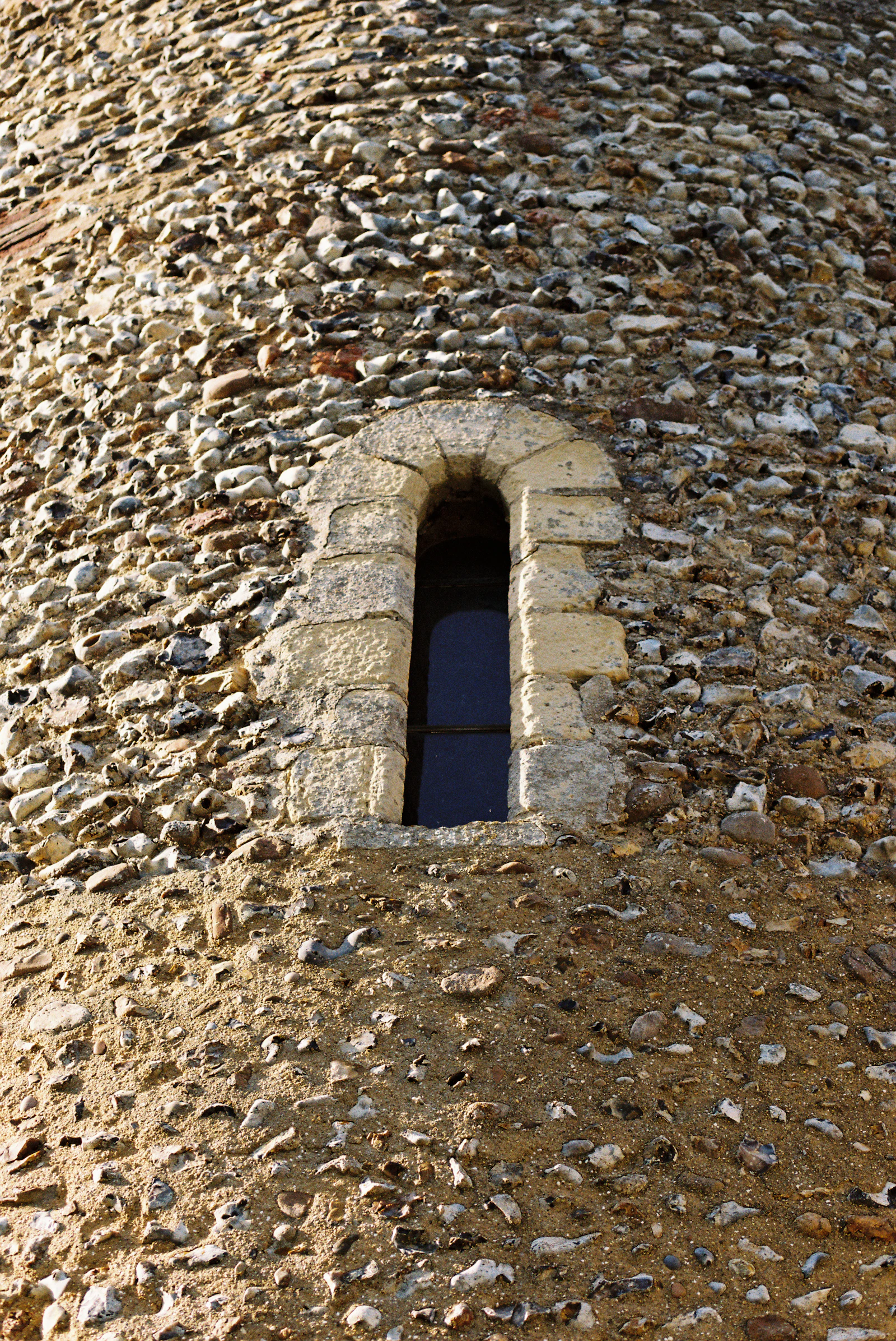 A small lancet window set deep in a flint and stone wall