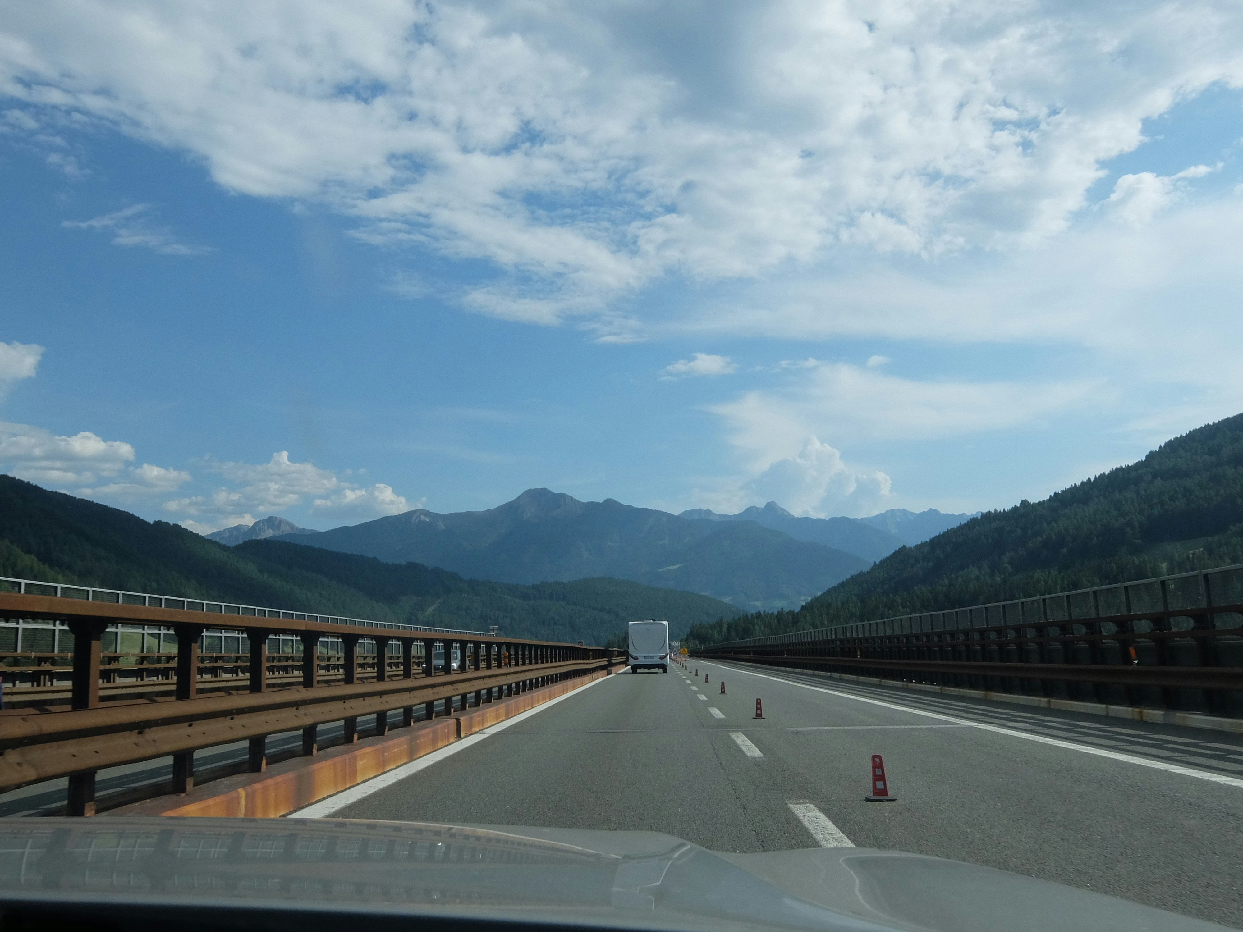 風光明媚な山々を高速道路で走り、前方にトラックが並んでいます。