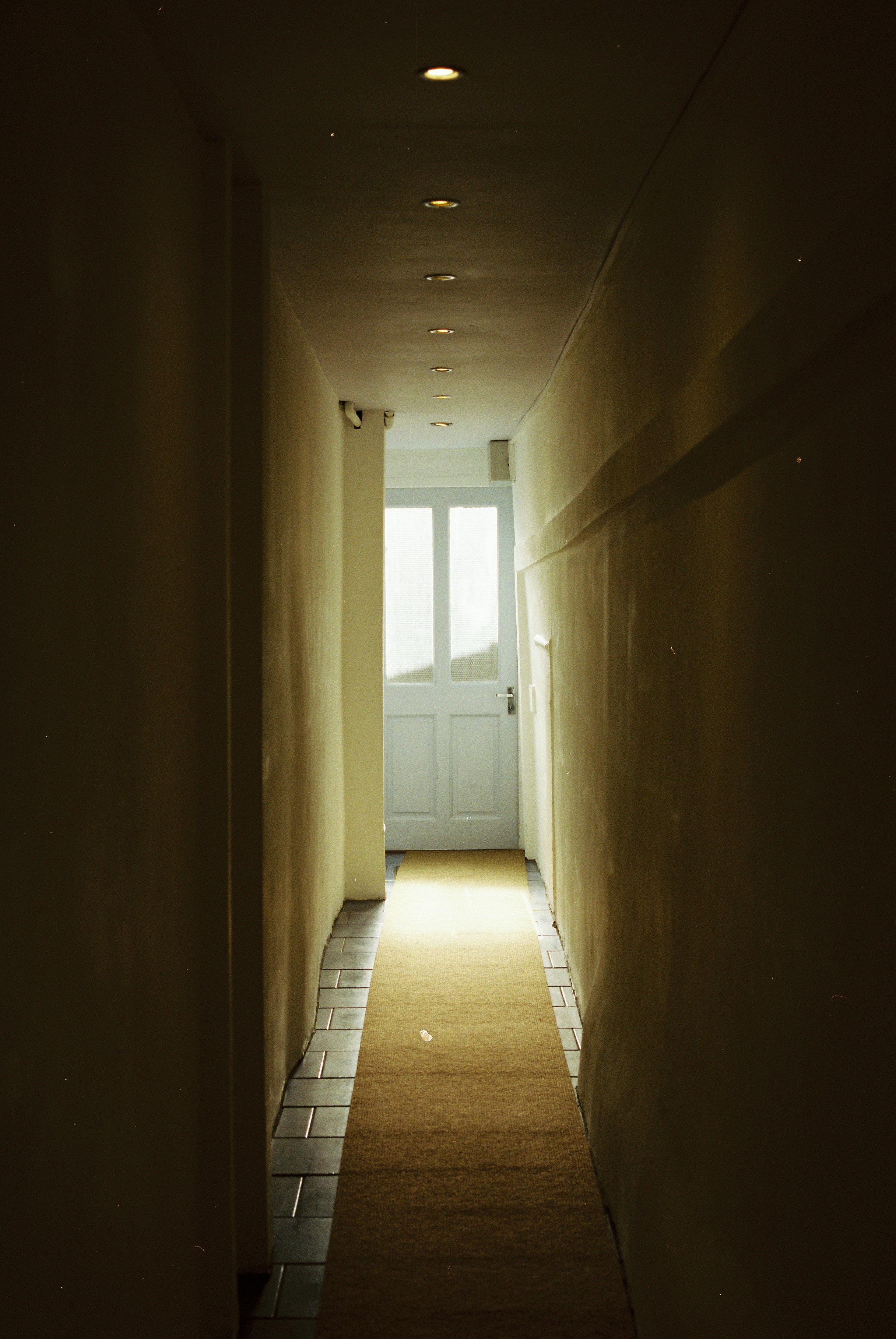 Long, dark hallway leading to a bright white door.