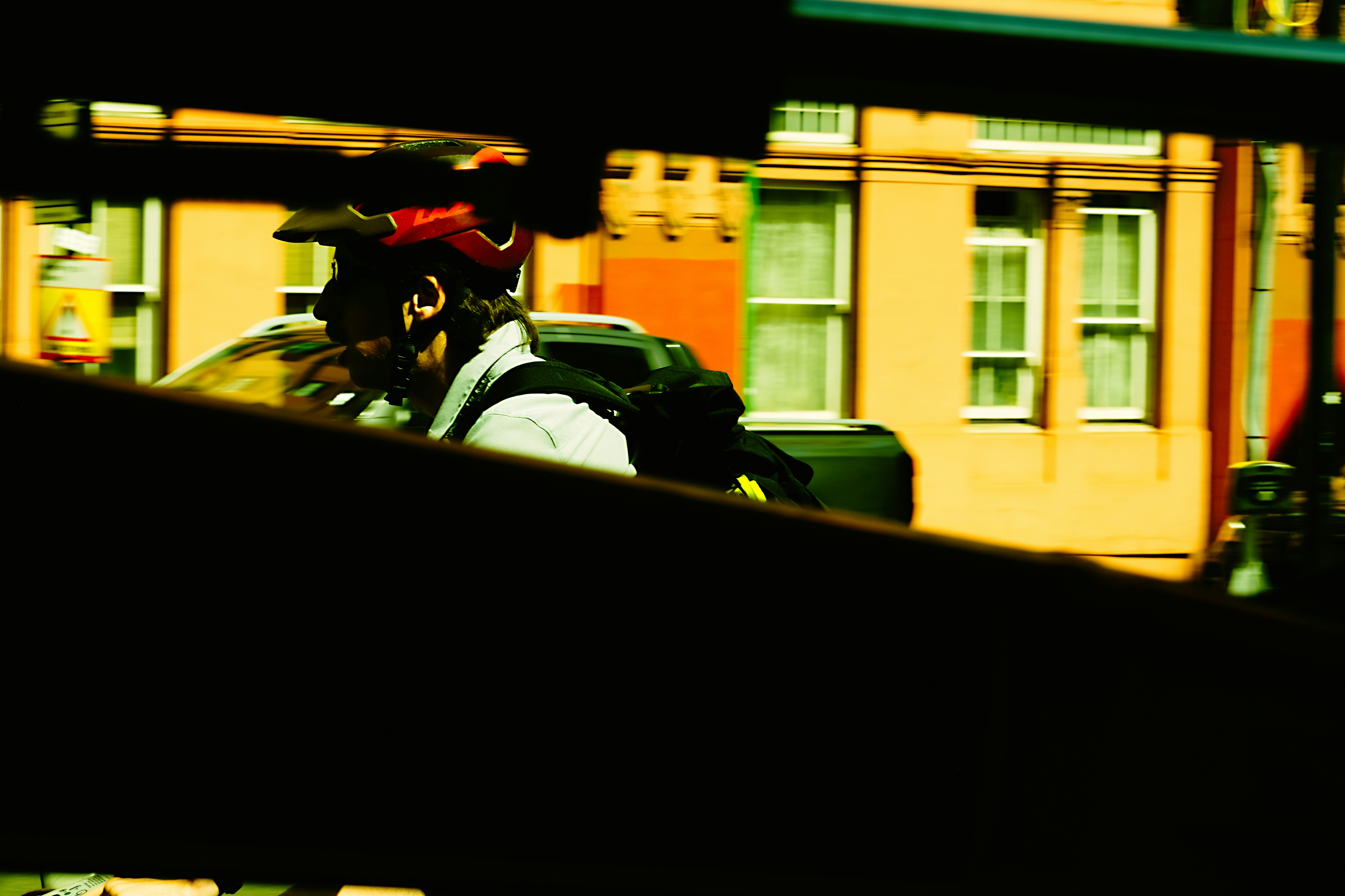 Cyclist with red helmet and backpack against an orange building.