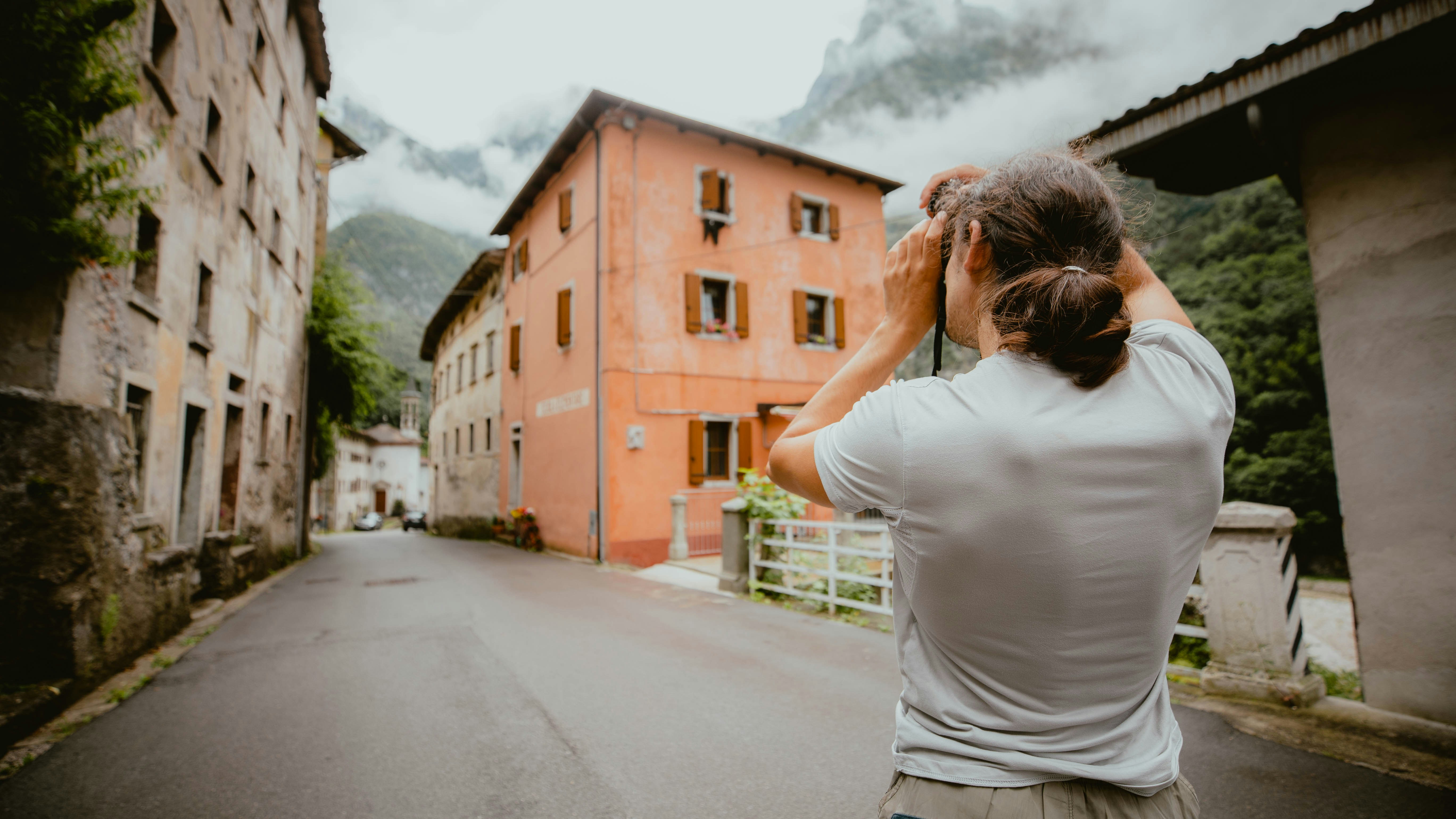 Man photographing historic buildings and misty mountains on a street.
