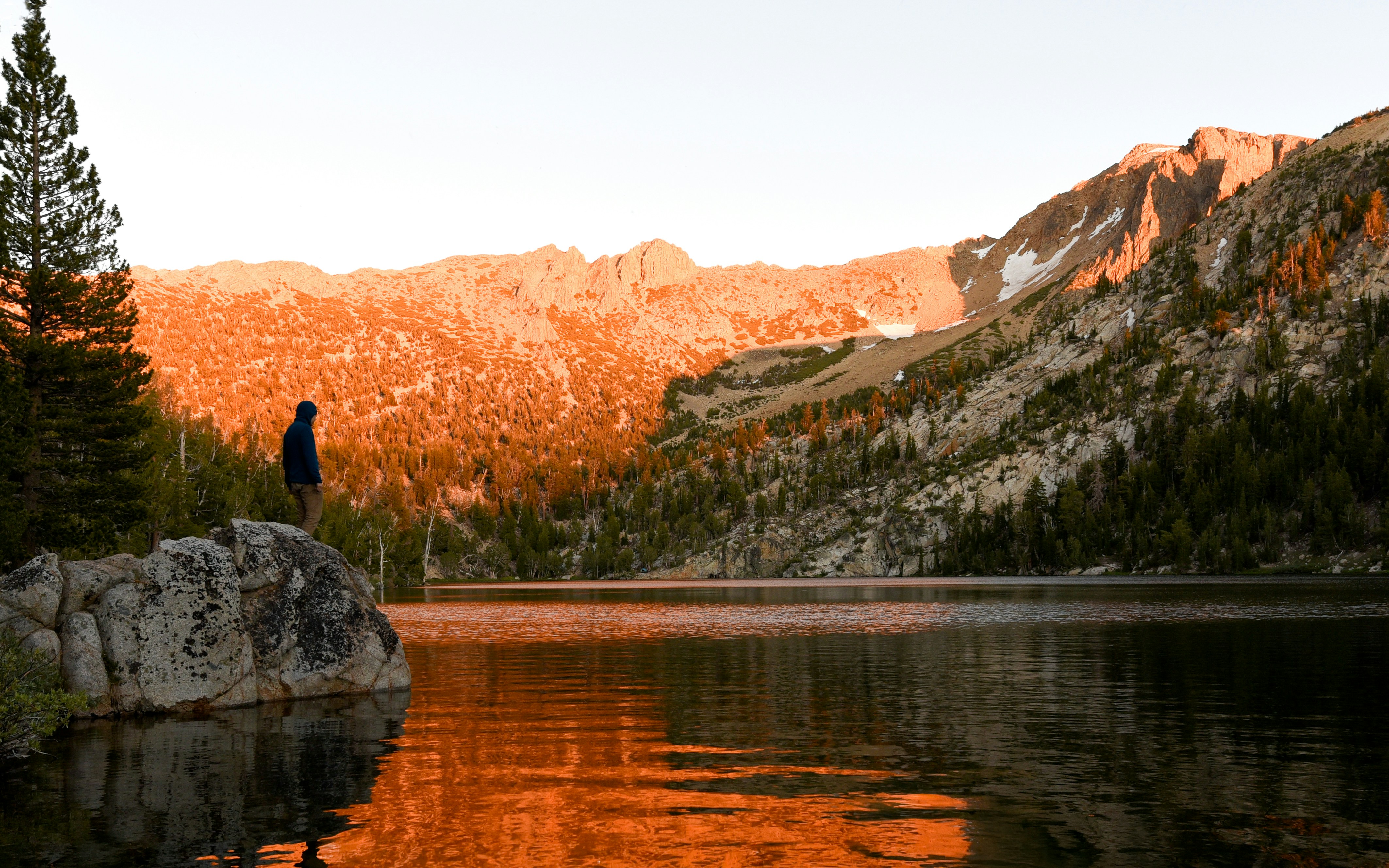 Person by serene lake with golden mountains at sunrise.