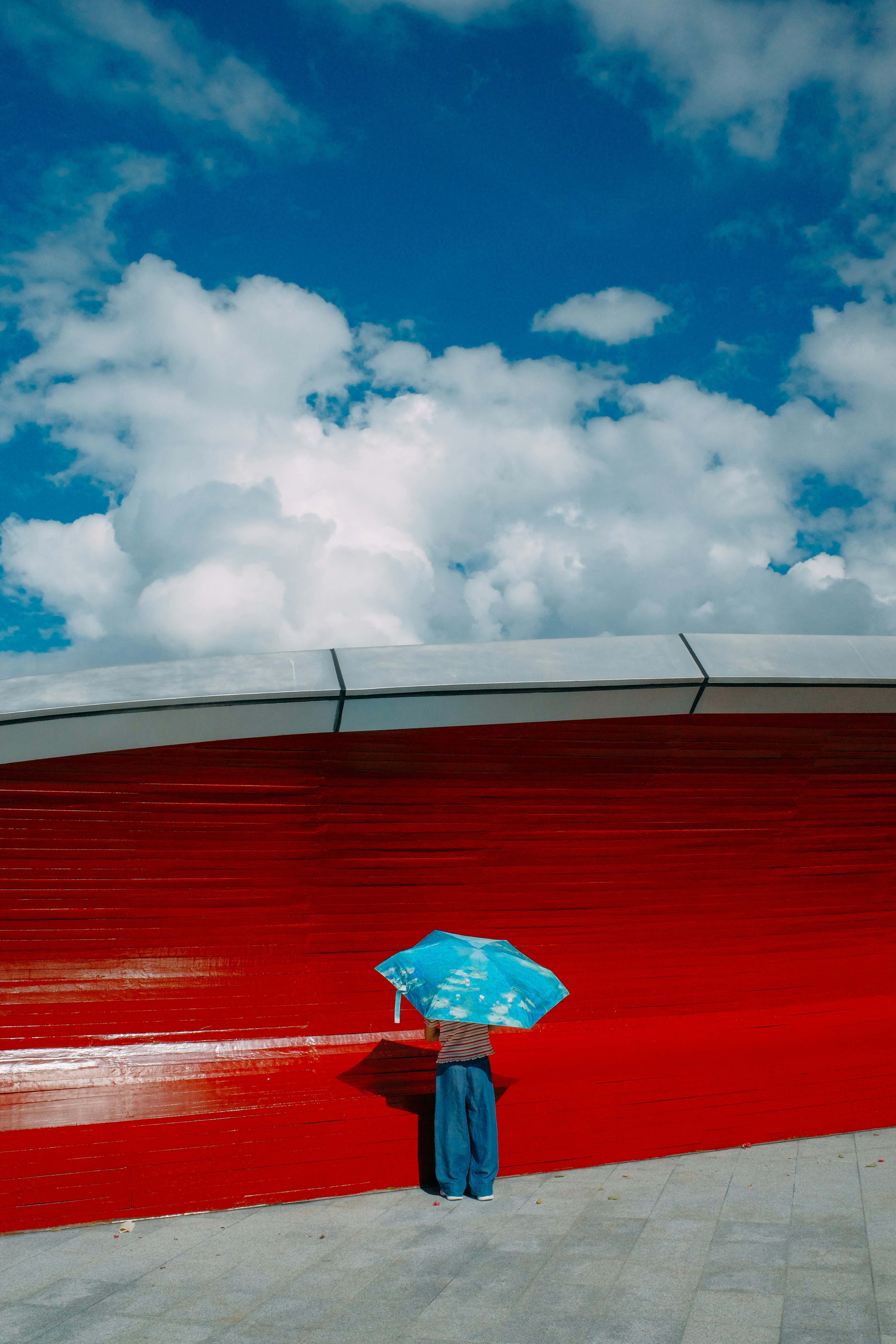 Blue umbrella against red wall under a cloudy blue sky.