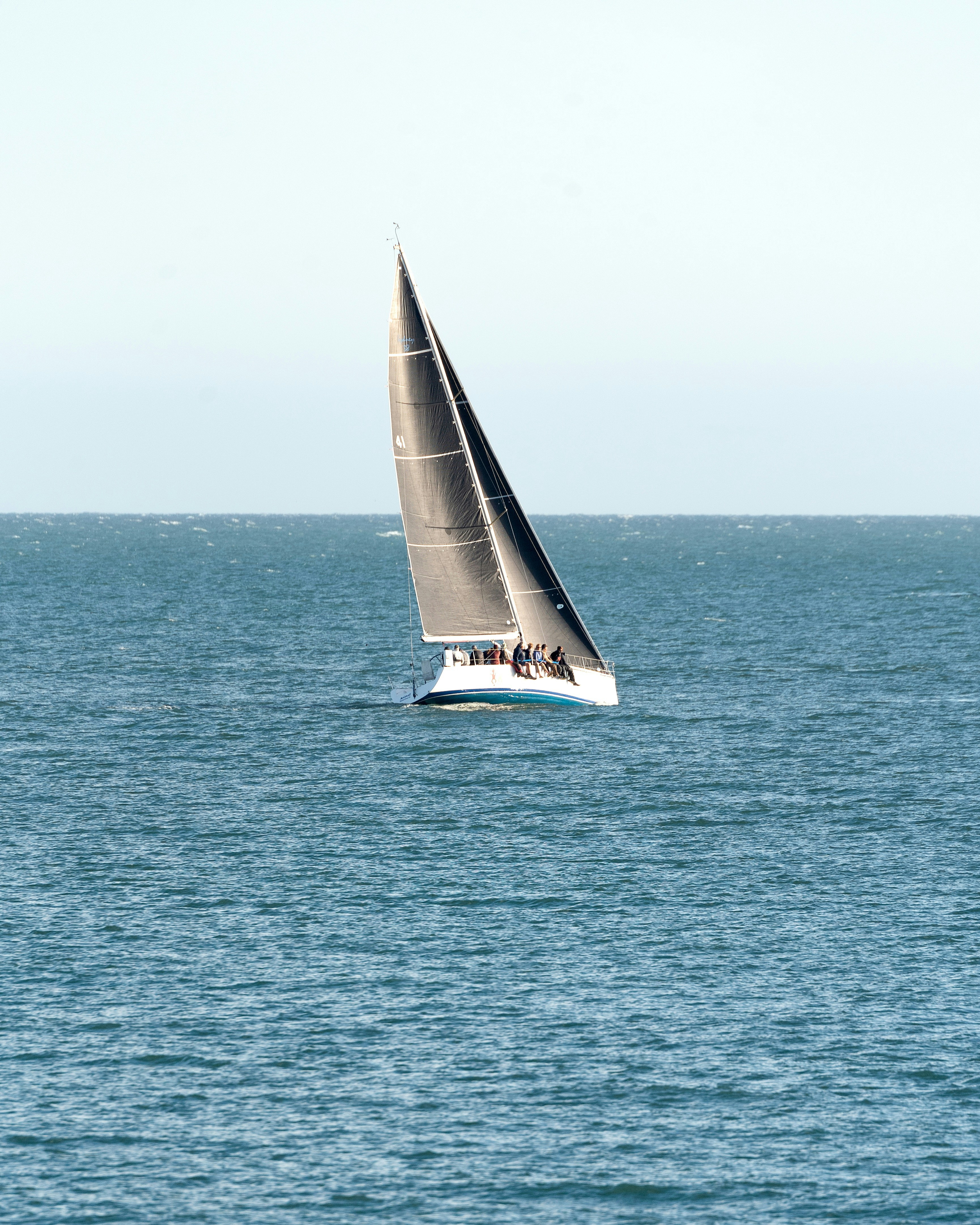 A sleek sailboat cruises on the calm blue water.