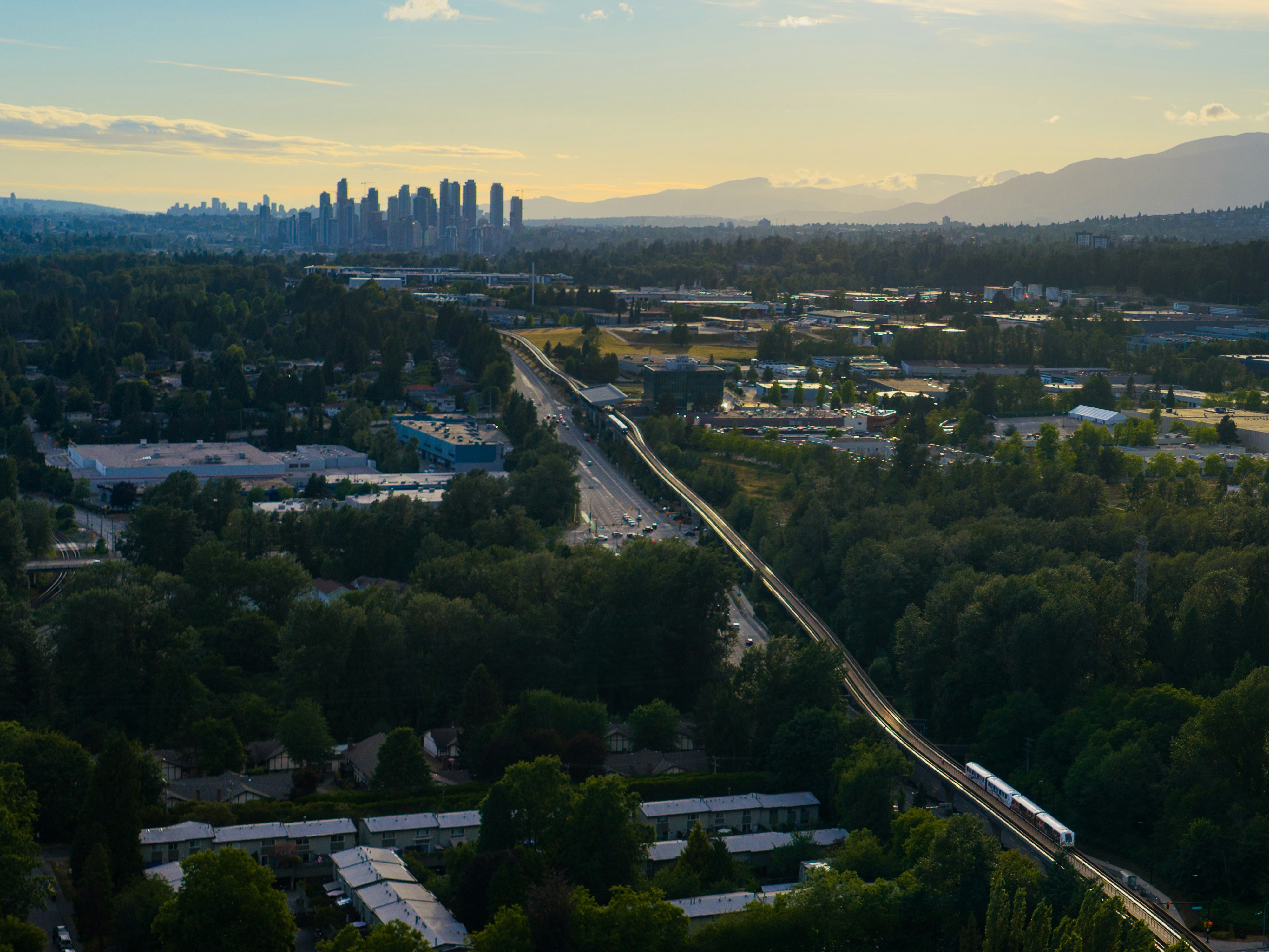 City skyline, elevated train, and green landscape at sunset.