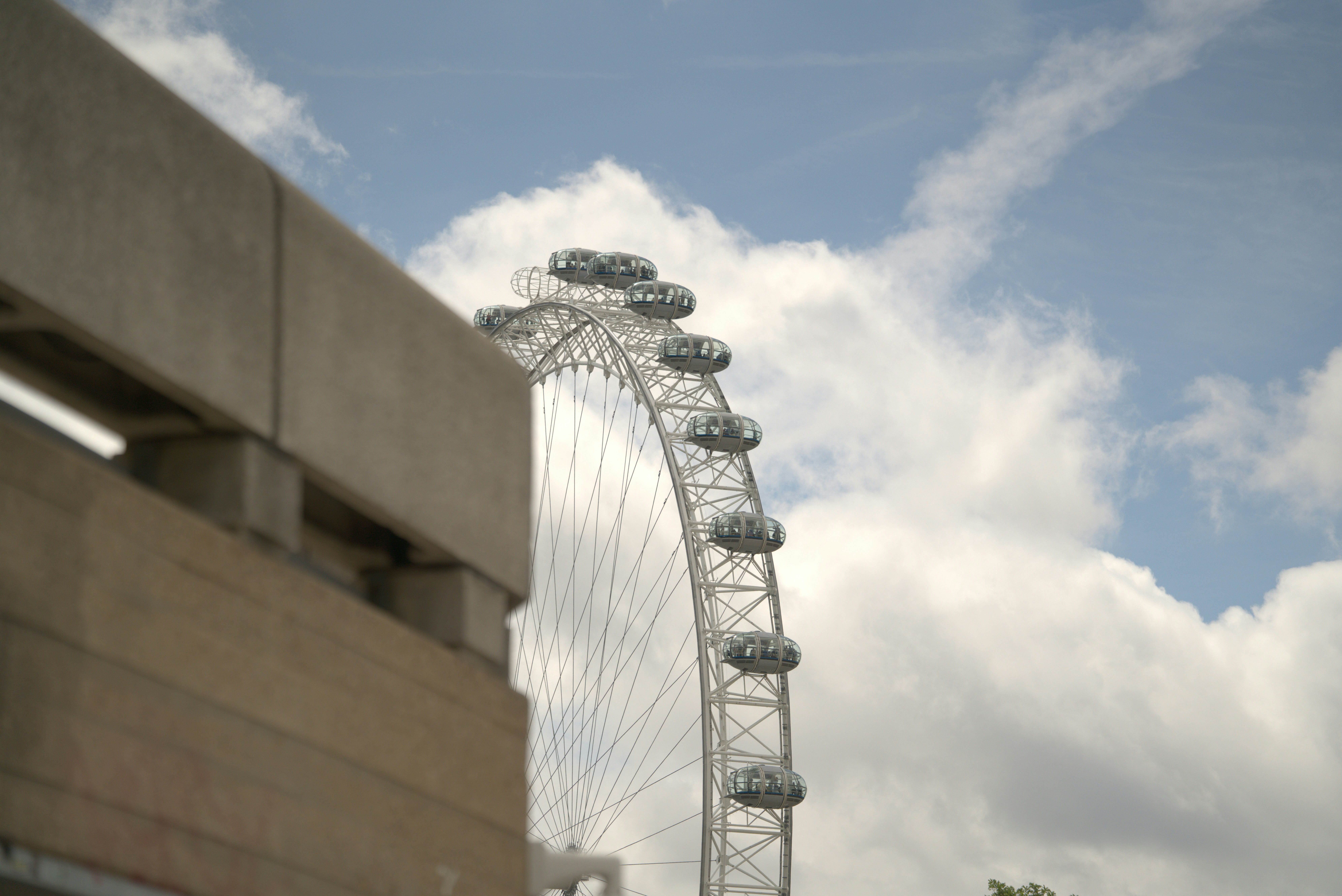 Large ferris wheel partially obscured by building under cloudy sky.