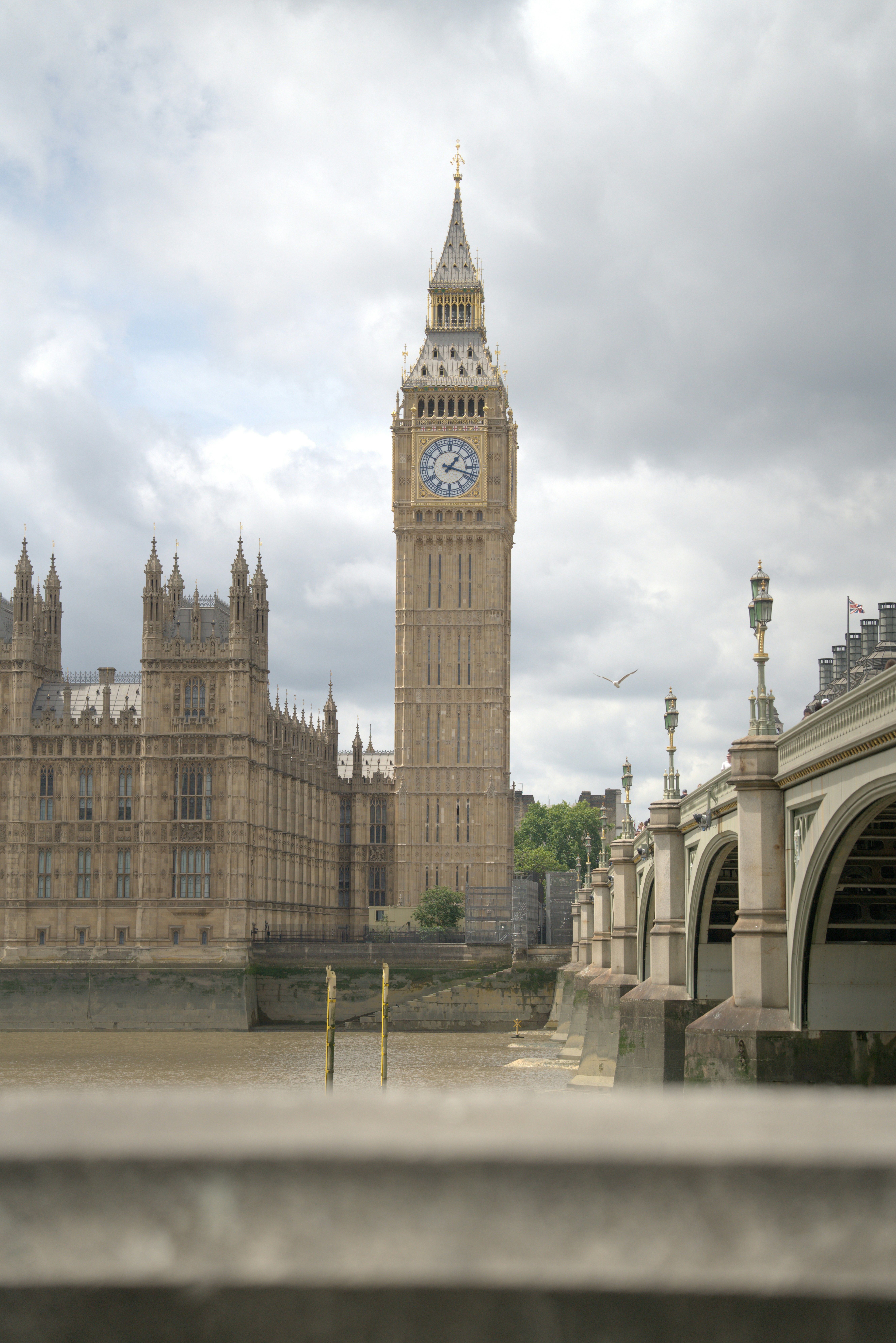 Big ben and parliament by river under cloudy sky.