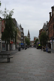 A quiet pedestrian street with buildings and a distant spire.