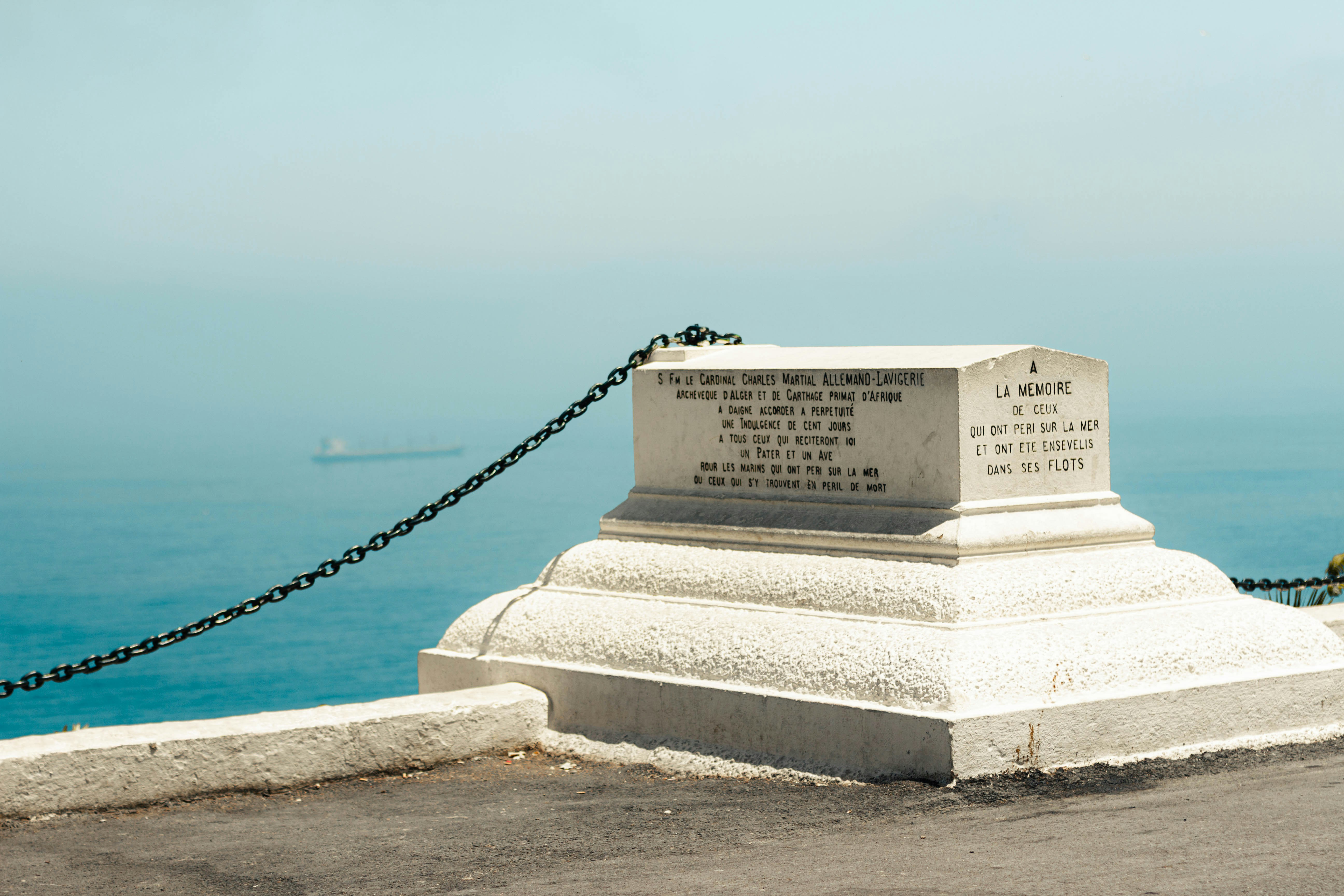 Monumento de piedra blanca con una valla de cadena que da al océano.