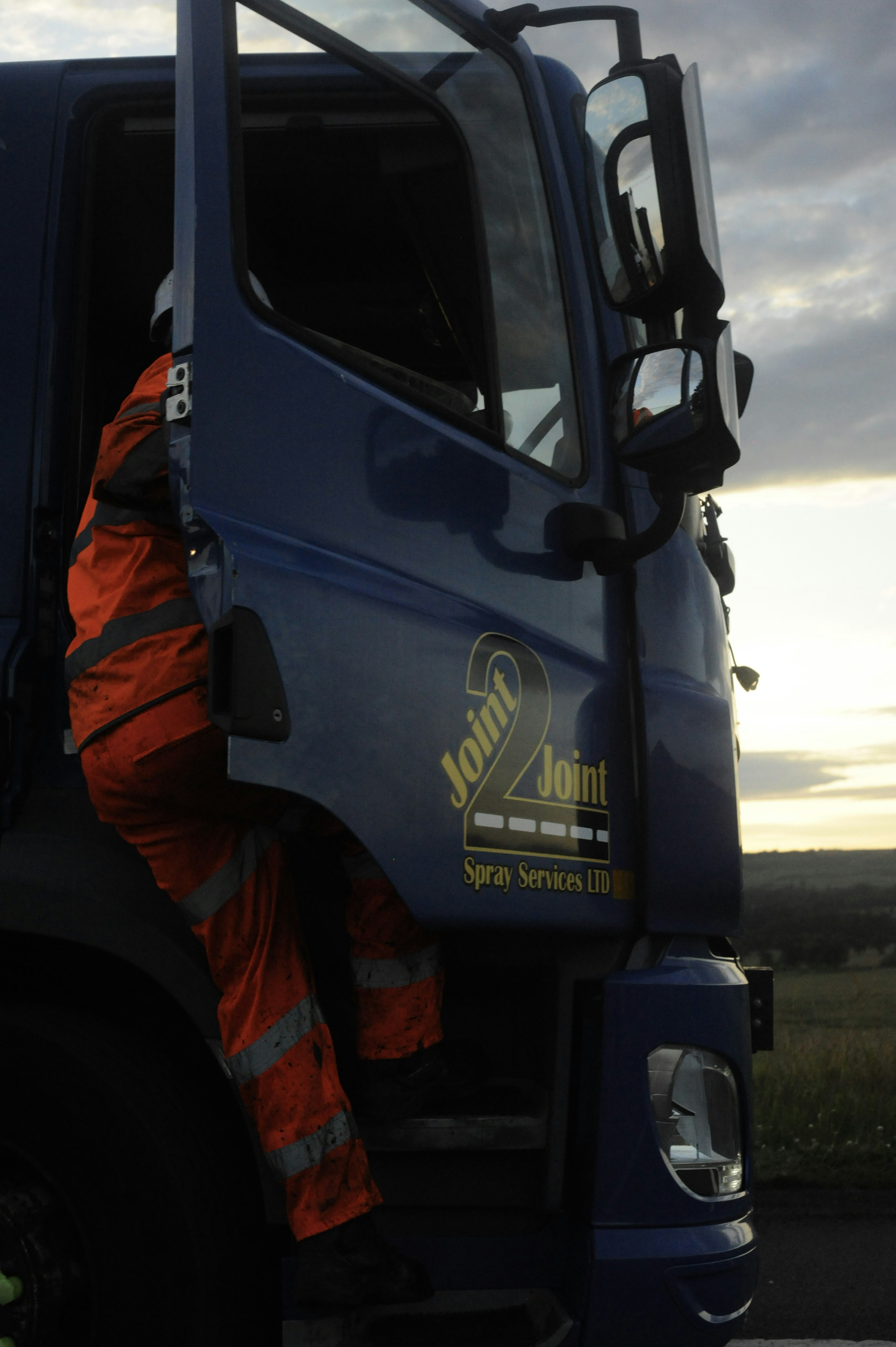 Worker in orange high-visibility gear entering a blue truck.
