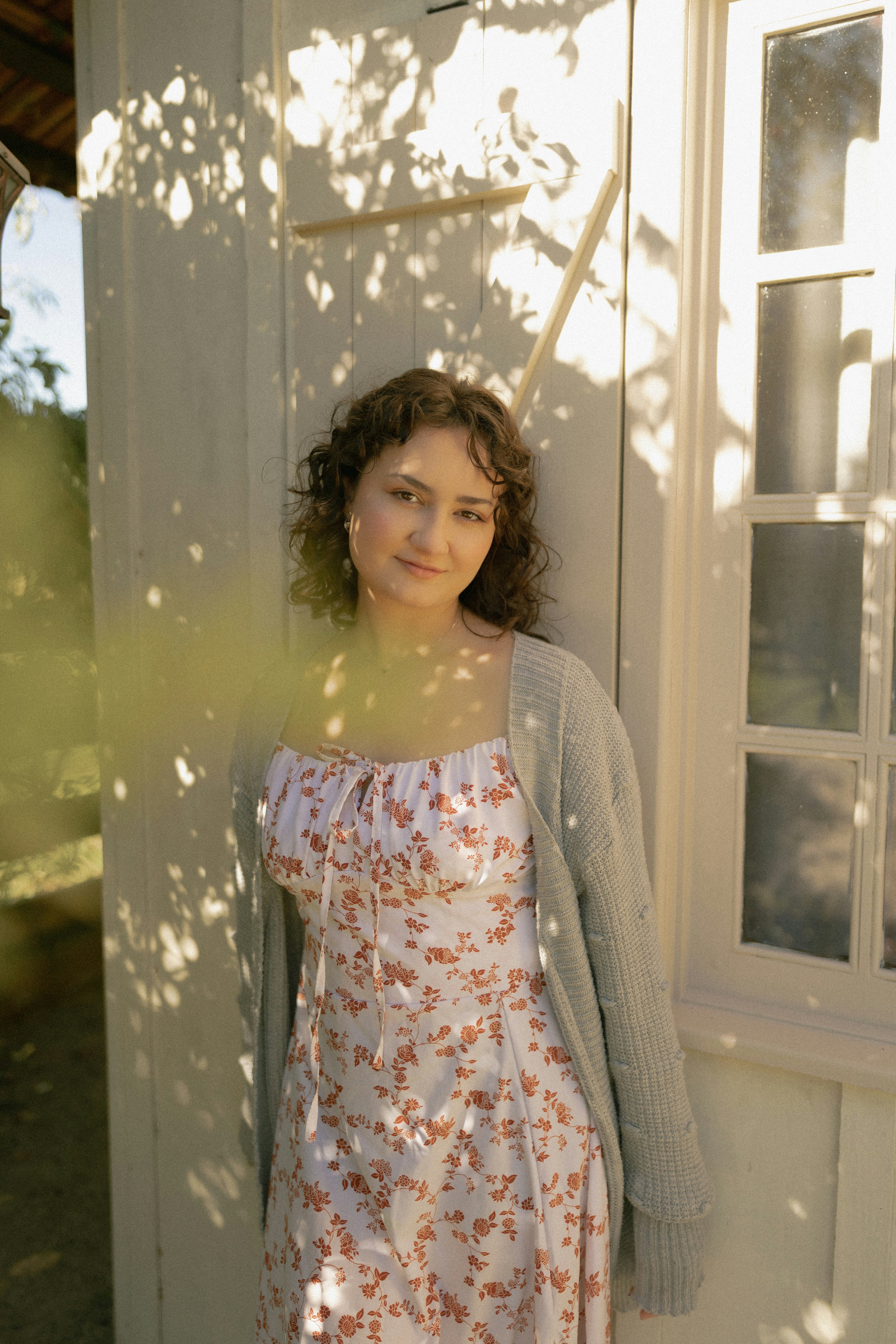 Young woman in floral dress and cardigan with dappled sunlight