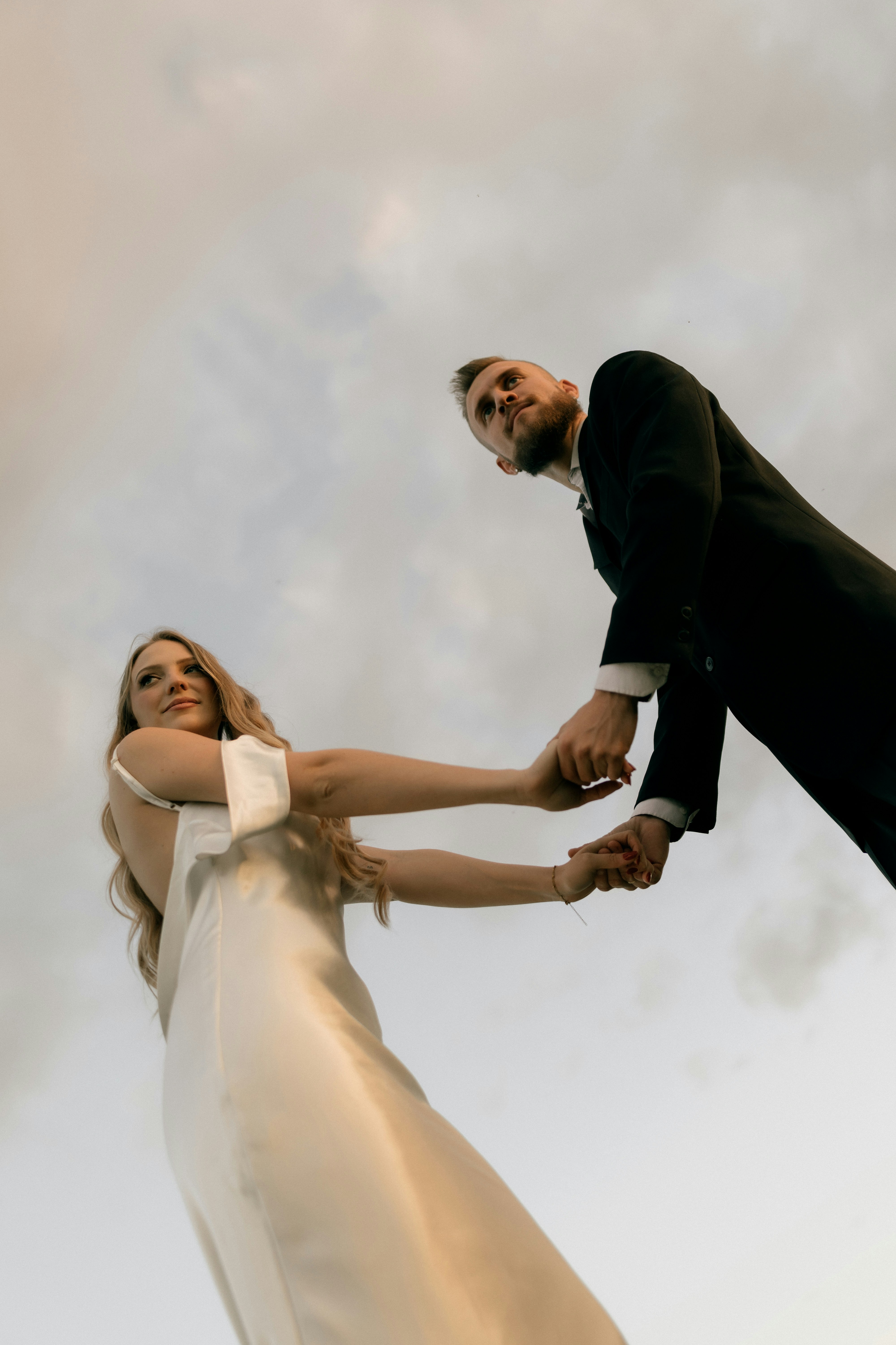 Una sposa e uno sposo che si tengono per mano sotto un cielo nuvoloso.