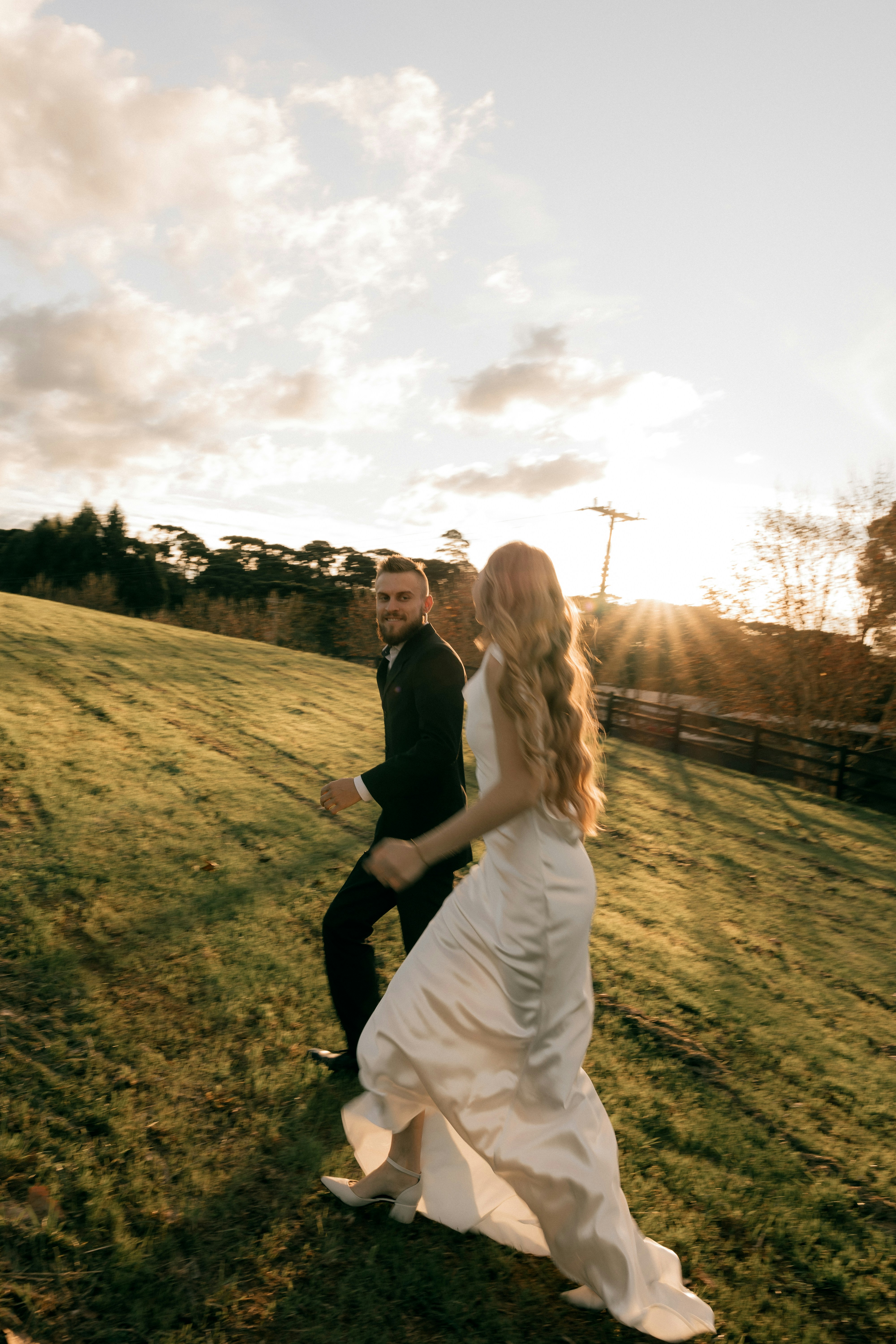 Sposa e sposo che camminano su per la collina al tramonto.