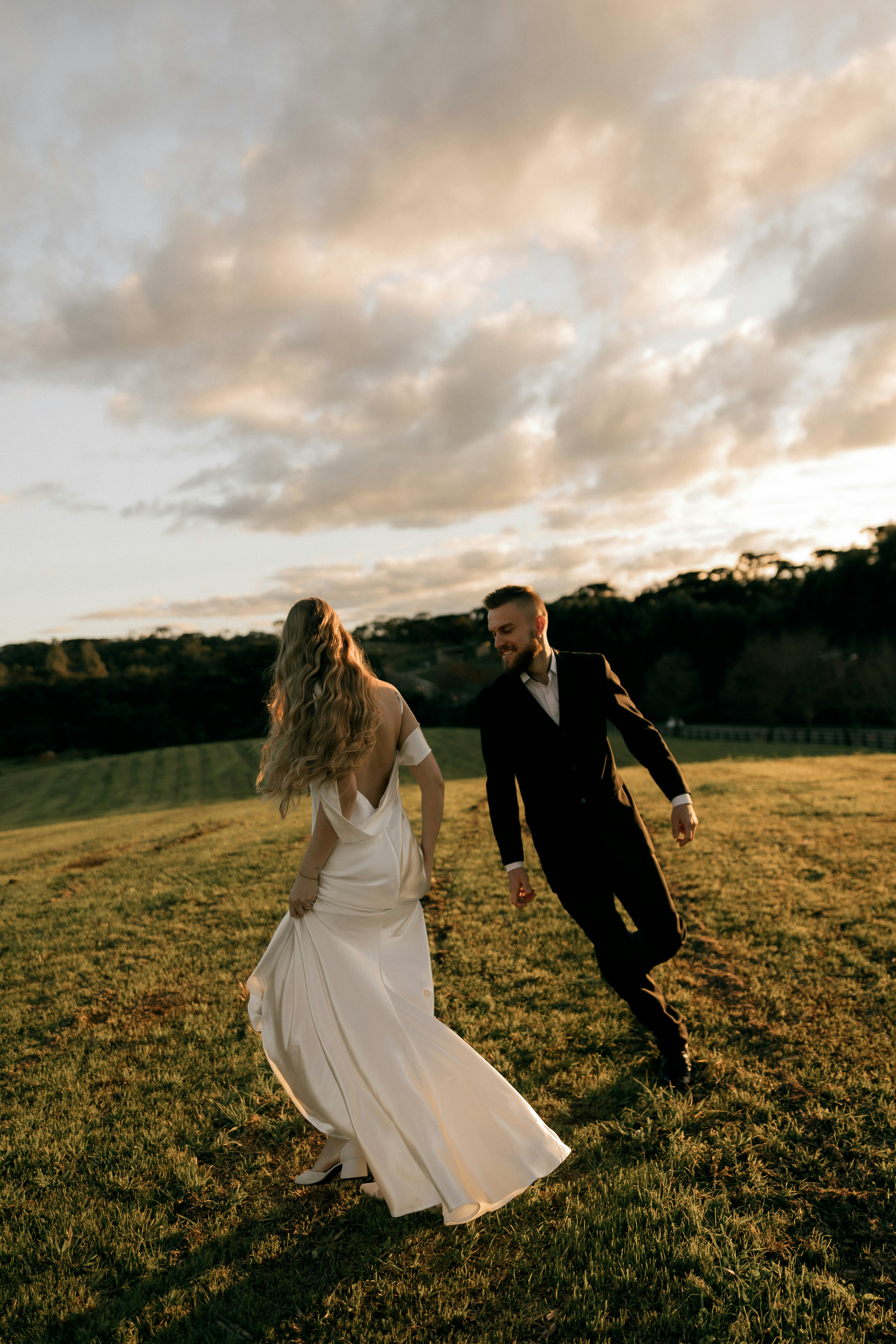 Una sposa e uno sposo che camminano in un campo al tramonto.